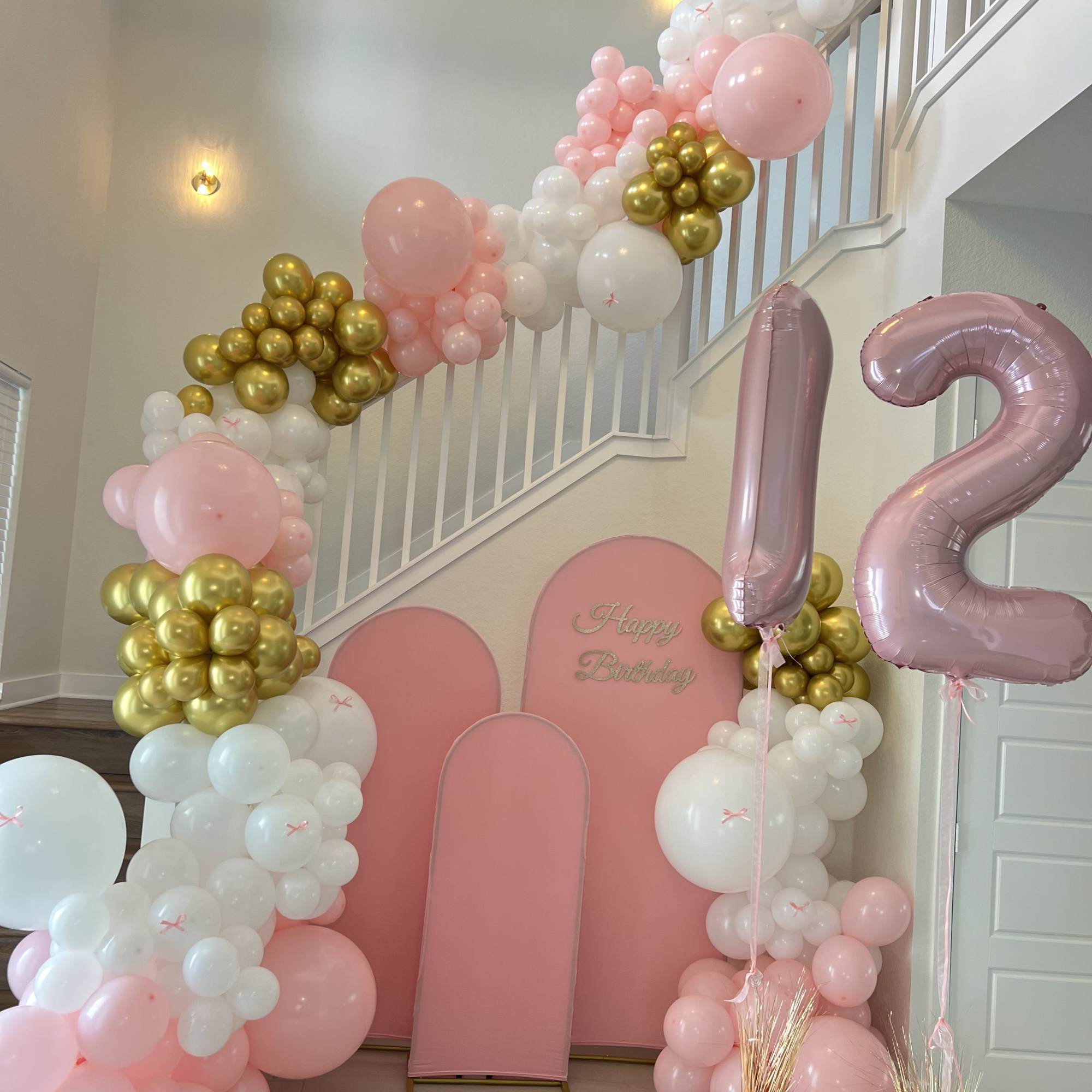 Pink, white, and gold balloon display with a large "12" and birthday backdrop