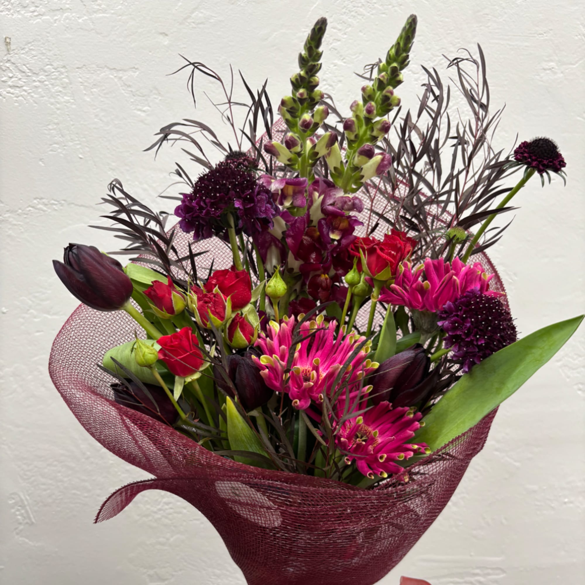 Bouquet of red and magenta flowers wrapped in burgundy mesh