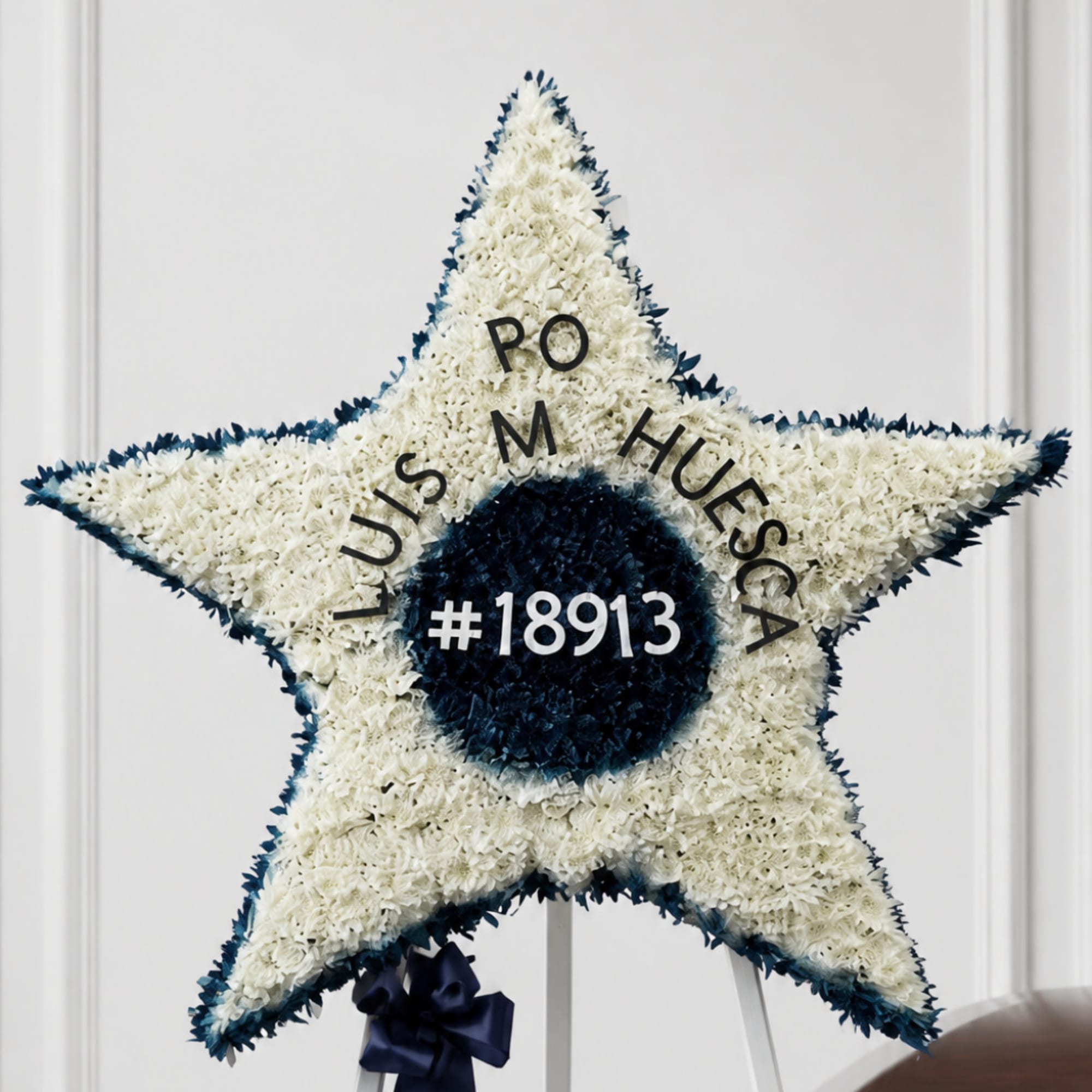 Star-shaped white floral tribute with dark blue center and lettering on an easel