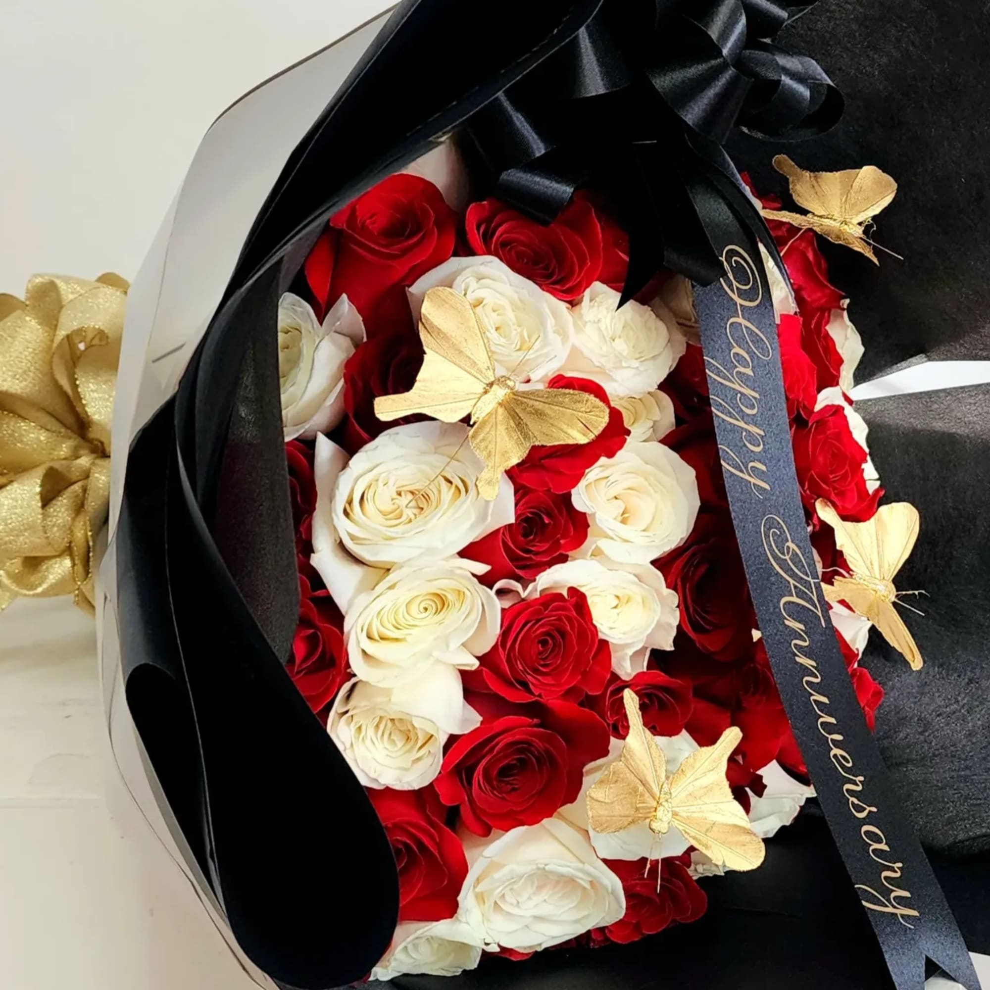 Bouquet of red and white roses wrapped in black paper with gold butterfly accents