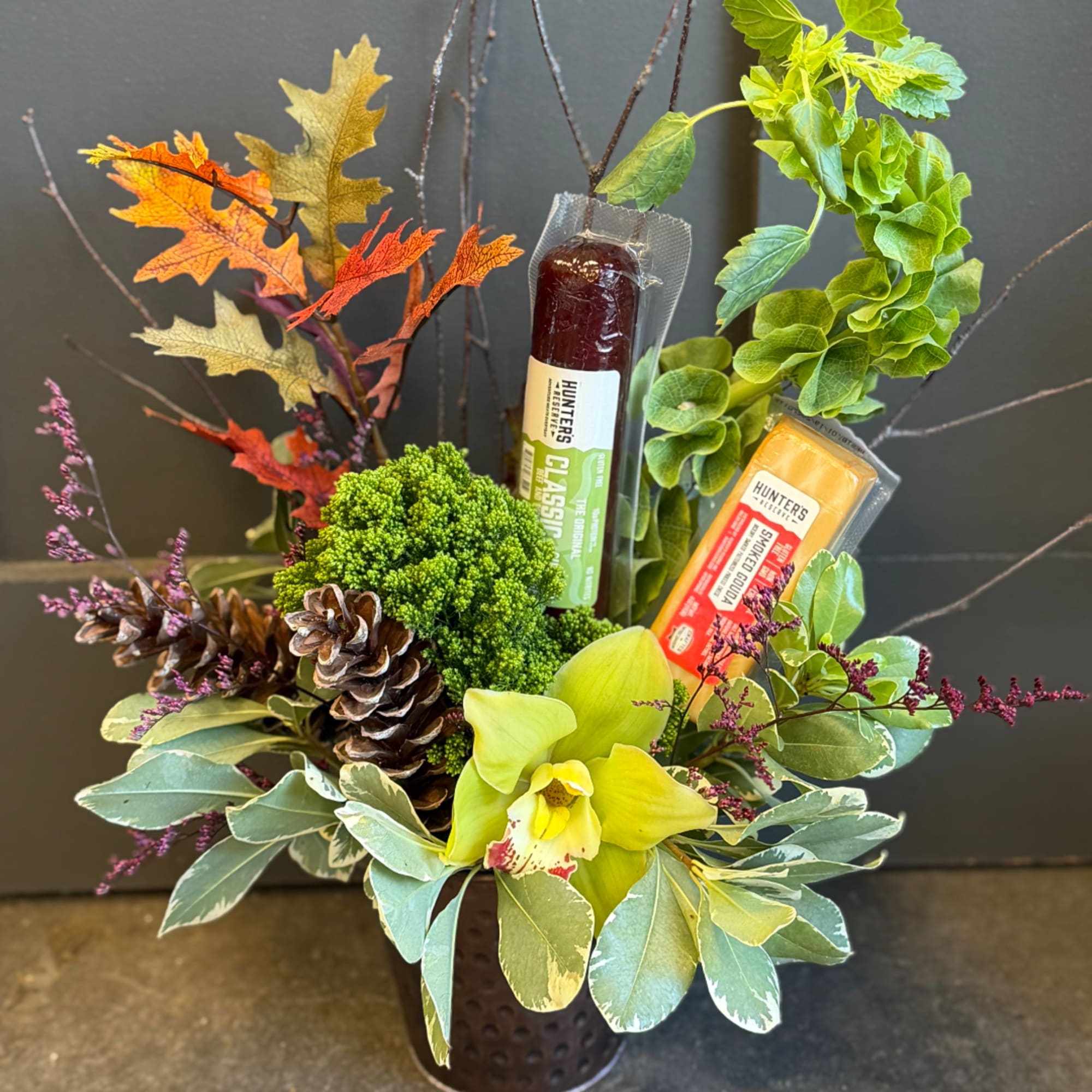 Autumn floral arrangement with an orchid, pinecones, and packaged candy bars in a vase.