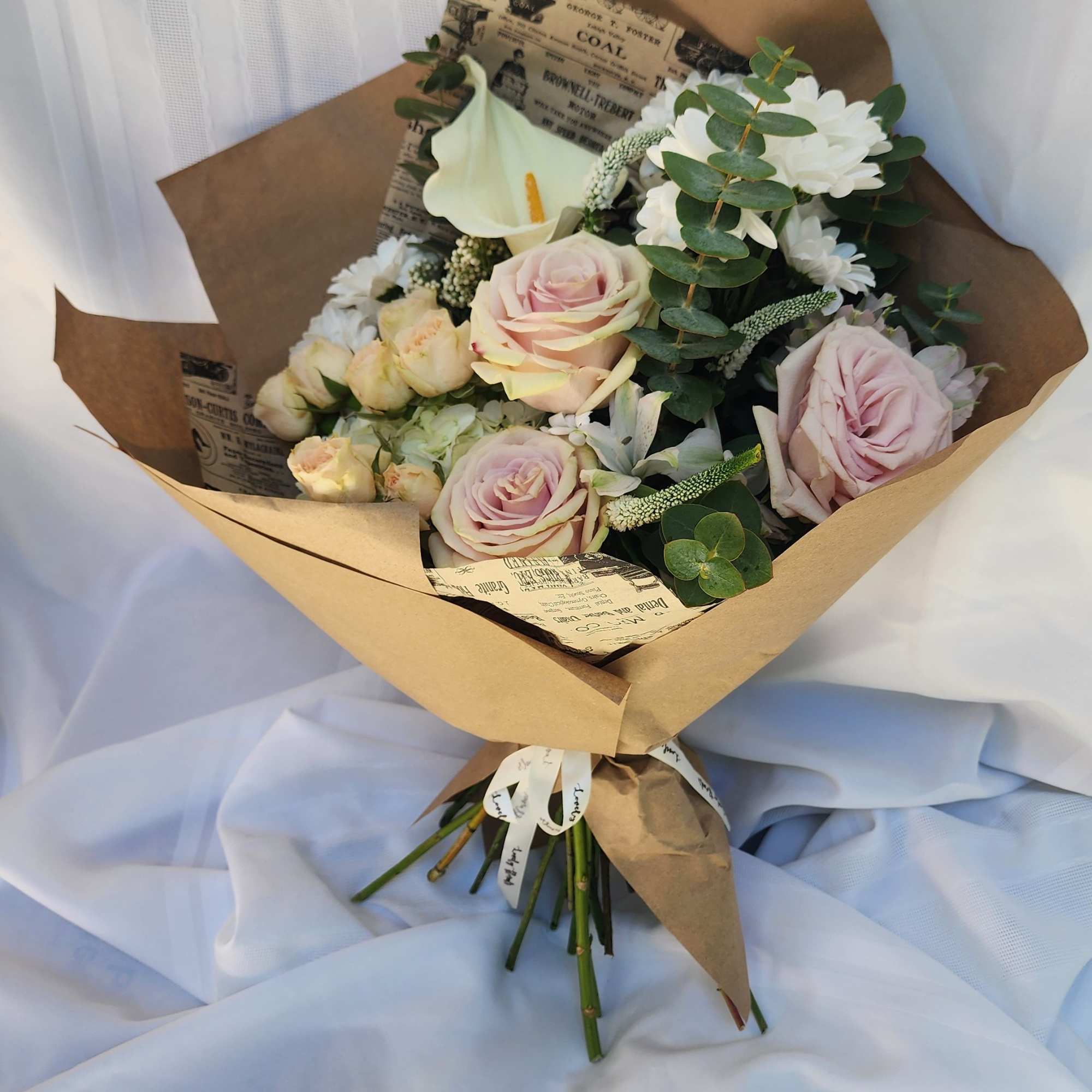 Bouquet of pale pink roses and white flowers wrapped in brown paper