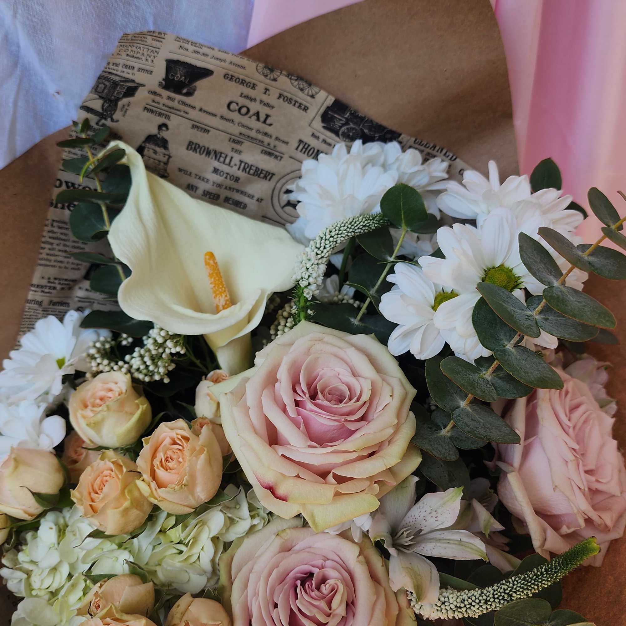 Bouquet of pink roses, white calla lily, and white daisies wrapped in brown paper