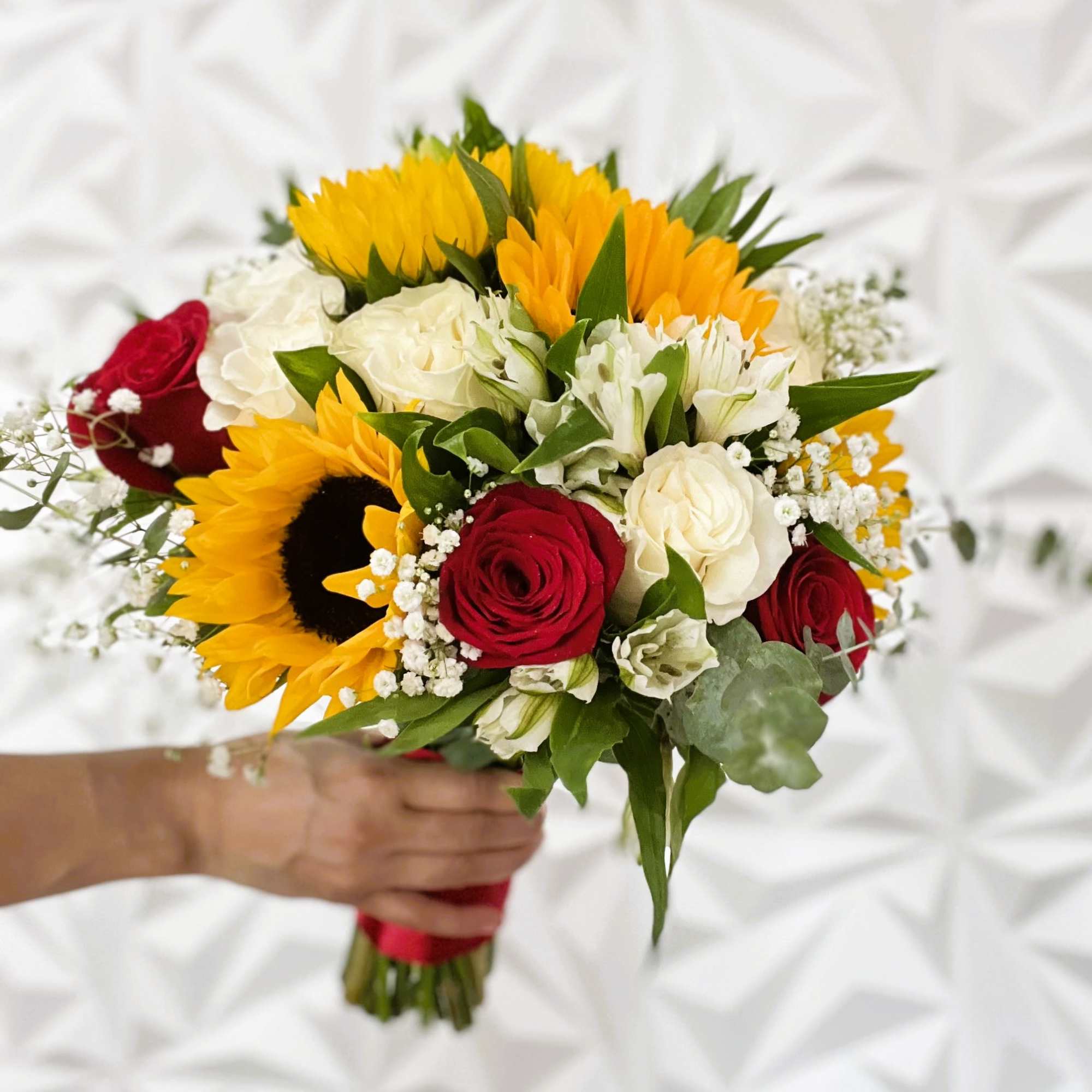 Handheld bouquet of red roses, white flowers, and sunflowers