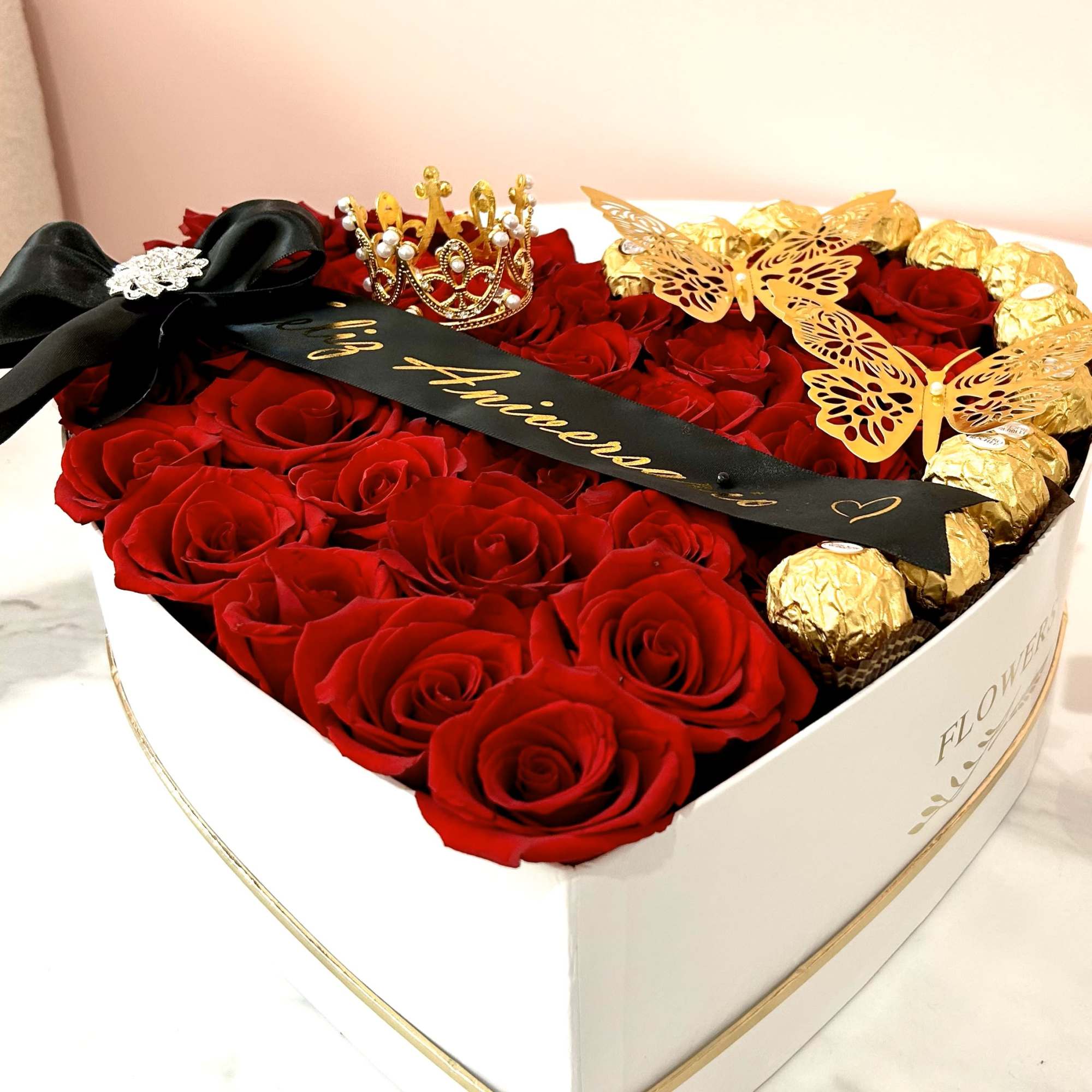 Heart-shaped box of red roses with gold-wrapped chocolates and a black ribbon