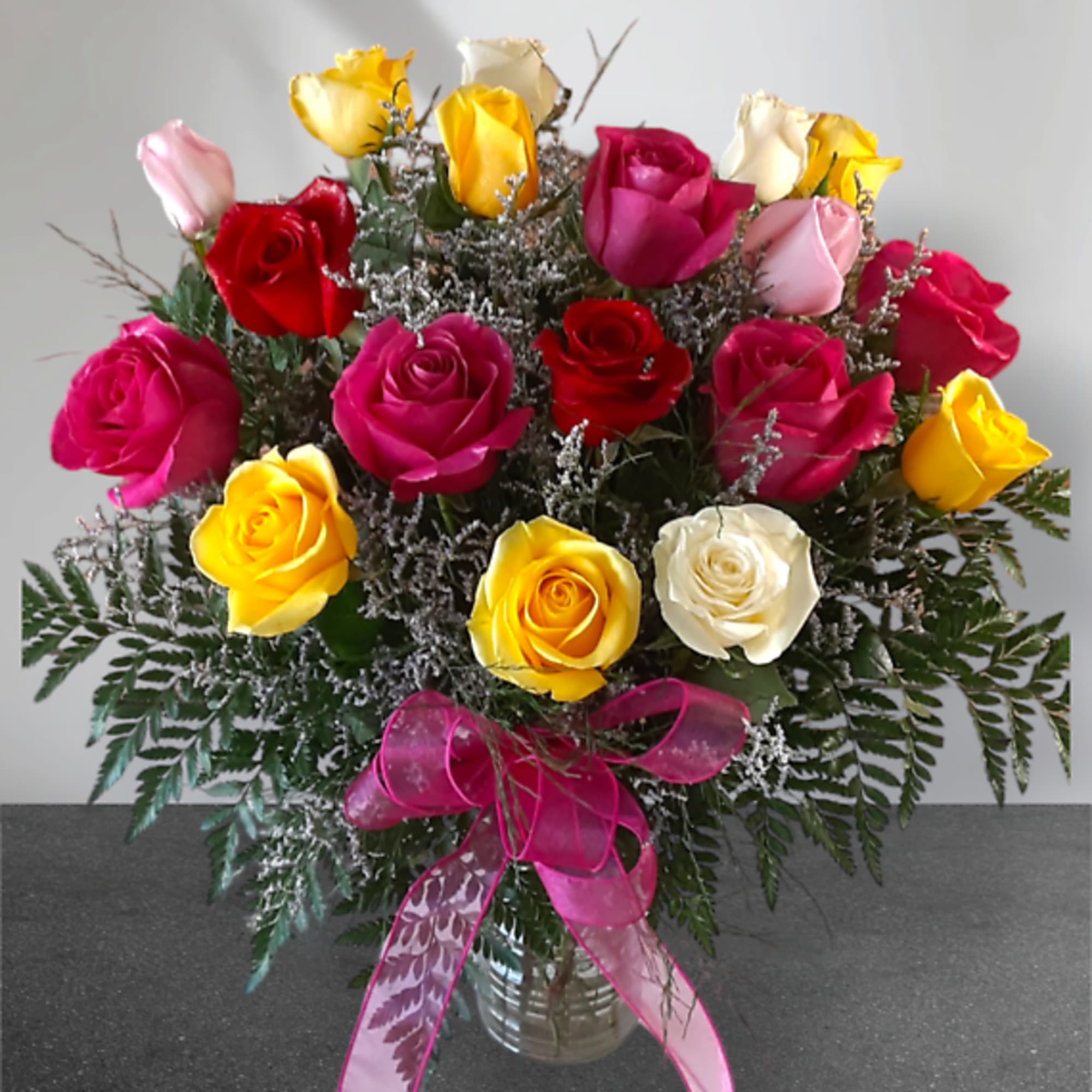 Bouquet of multicolored roses in a glass vase with a pink ribbon