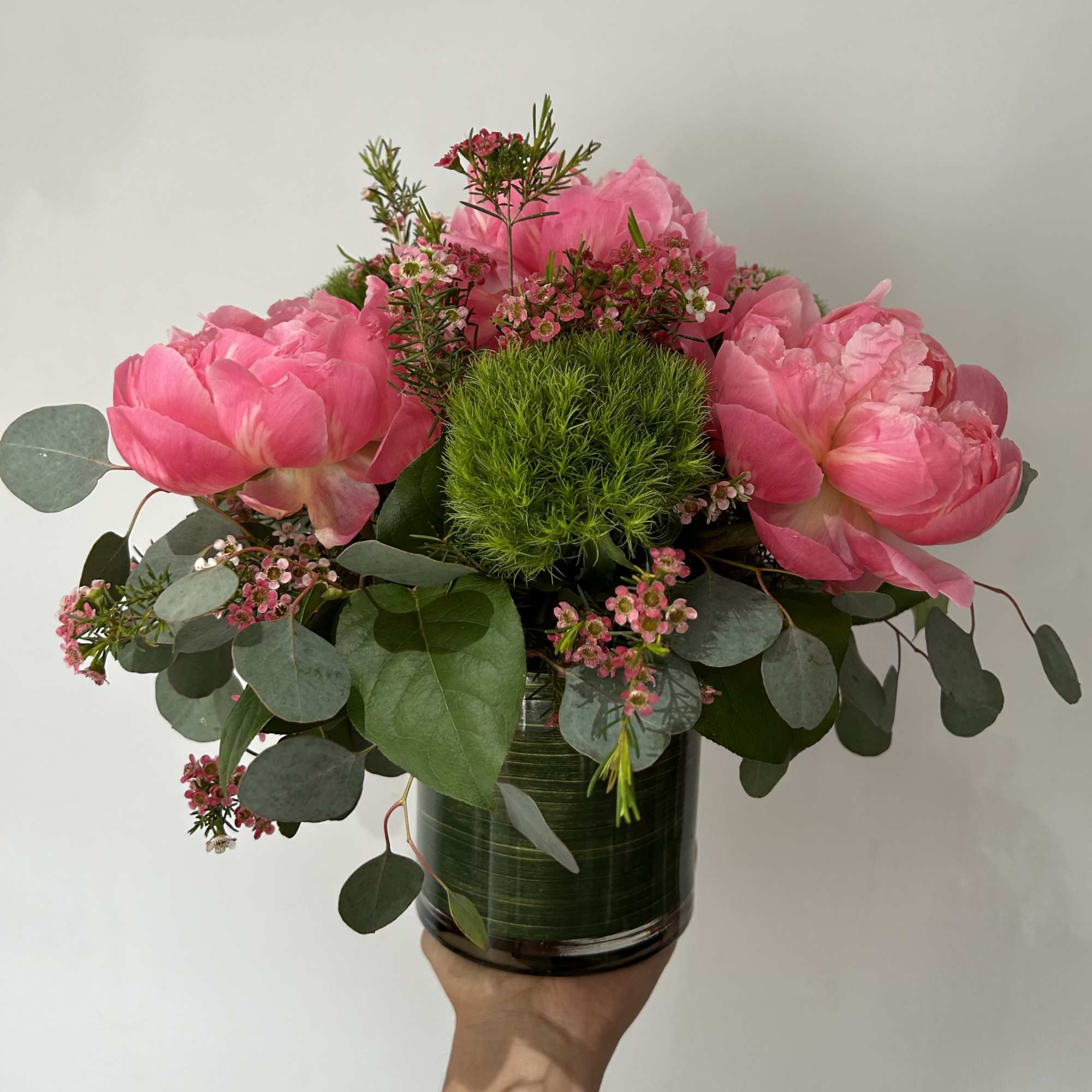 Seasonal peonies arranged with fillers and greens in a vase. 