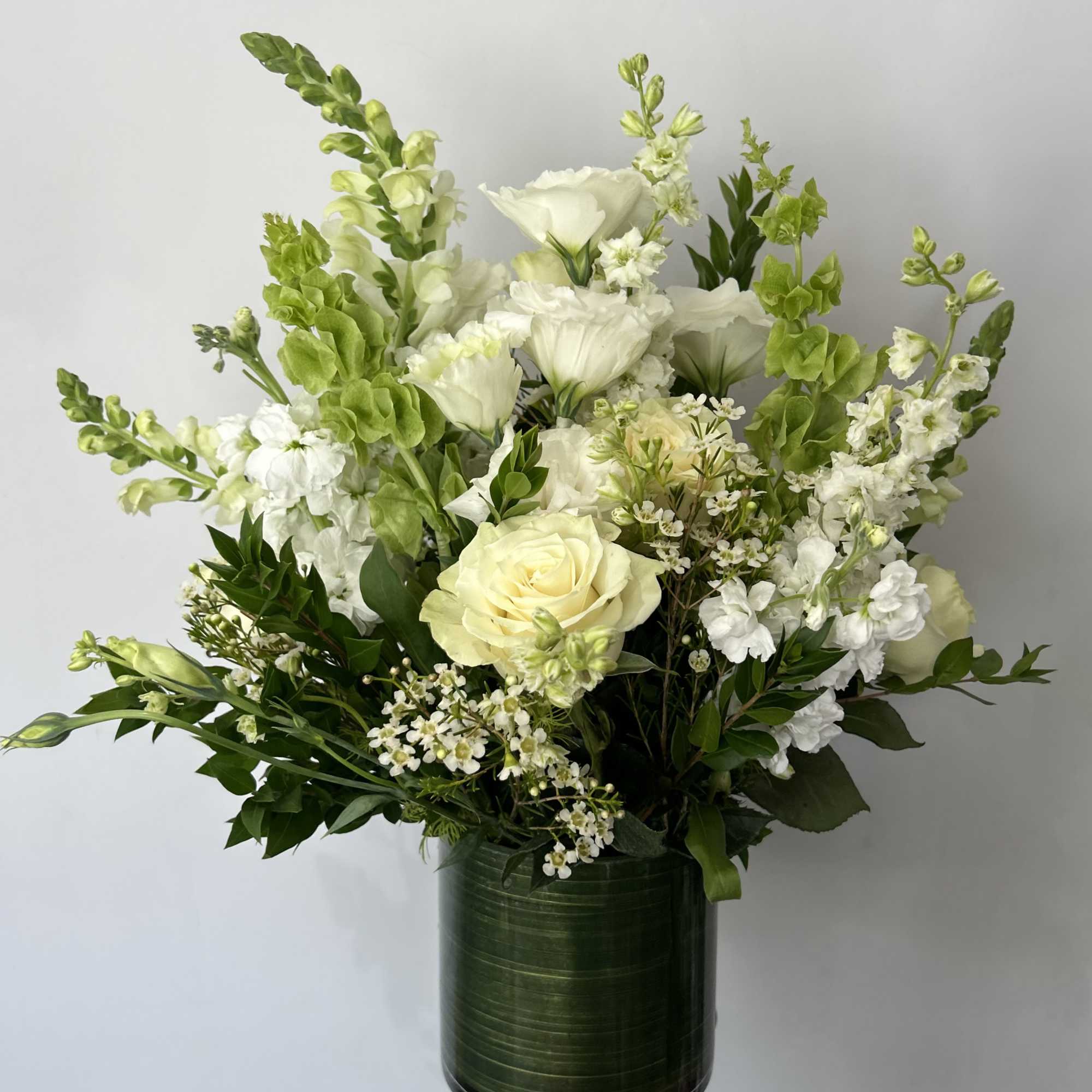 Seasonal white flowers arranged with fillers and greens in a vase.