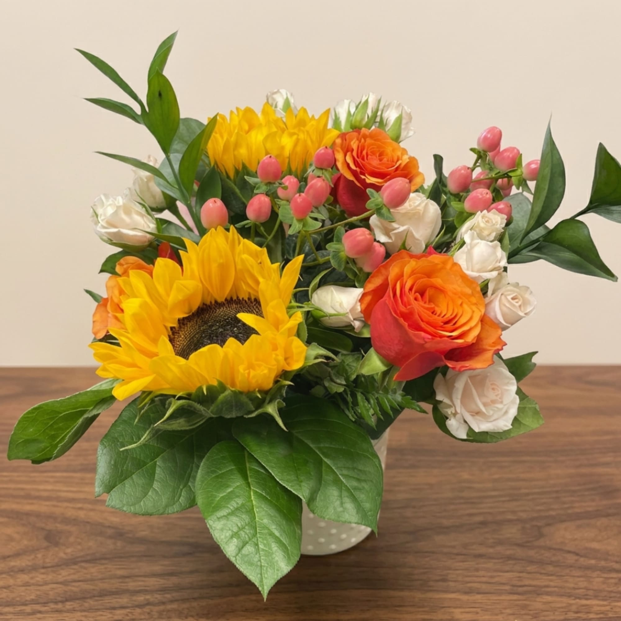 Sunflowers, orange roses, and white spray roses in a white vase