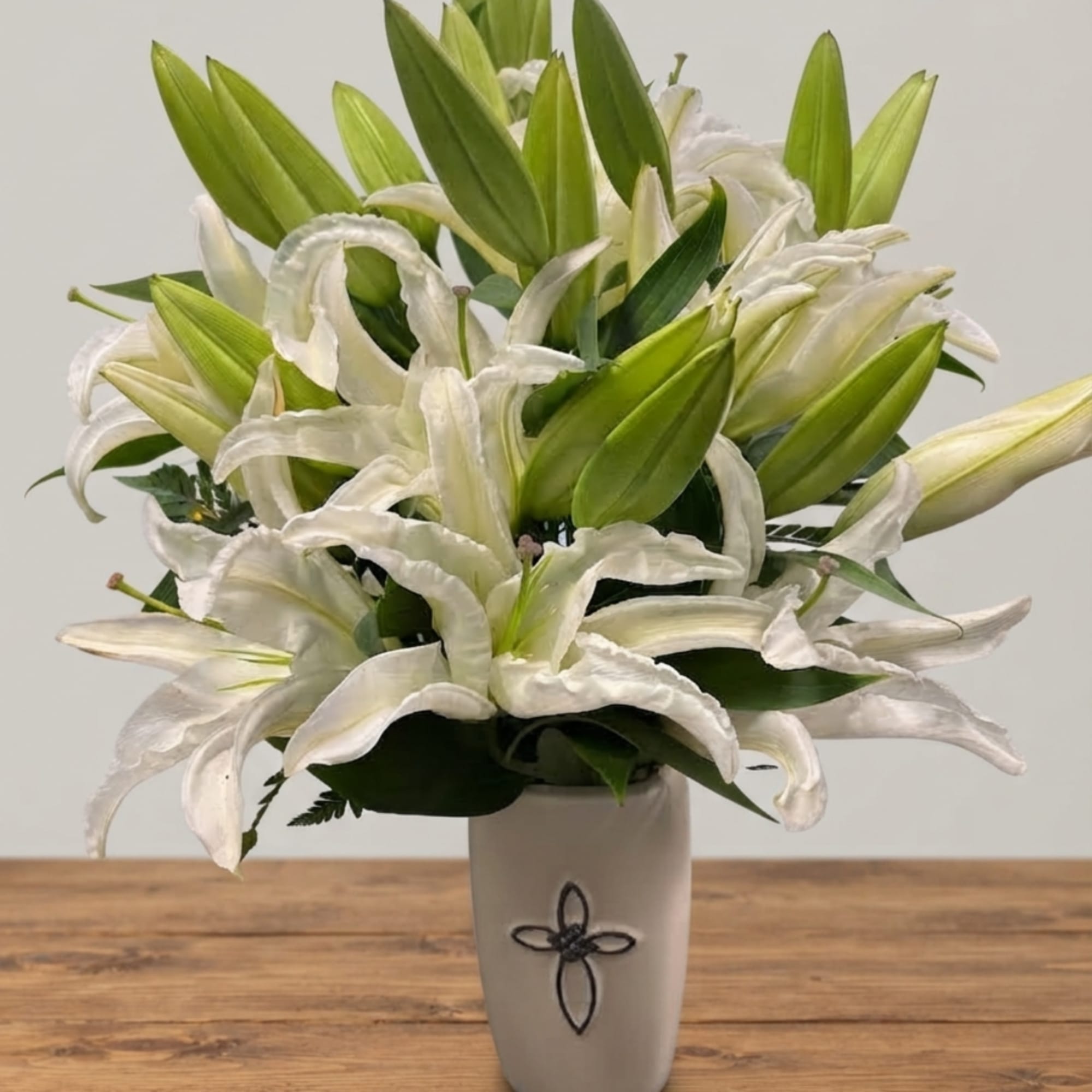 White lilies arranged in a tall white vase on a wooden table