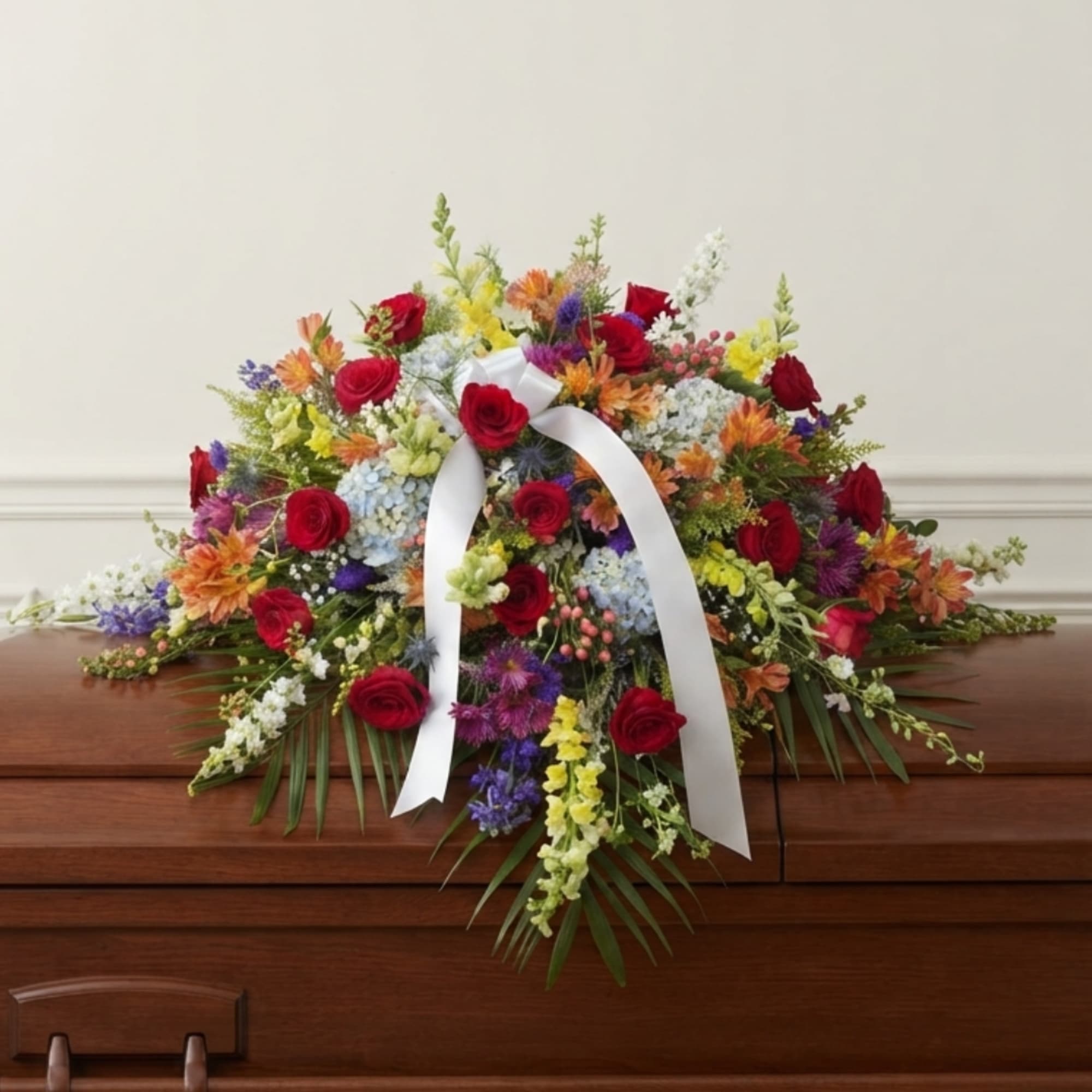 Colorful floral casket spray with red roses and a white ribbon