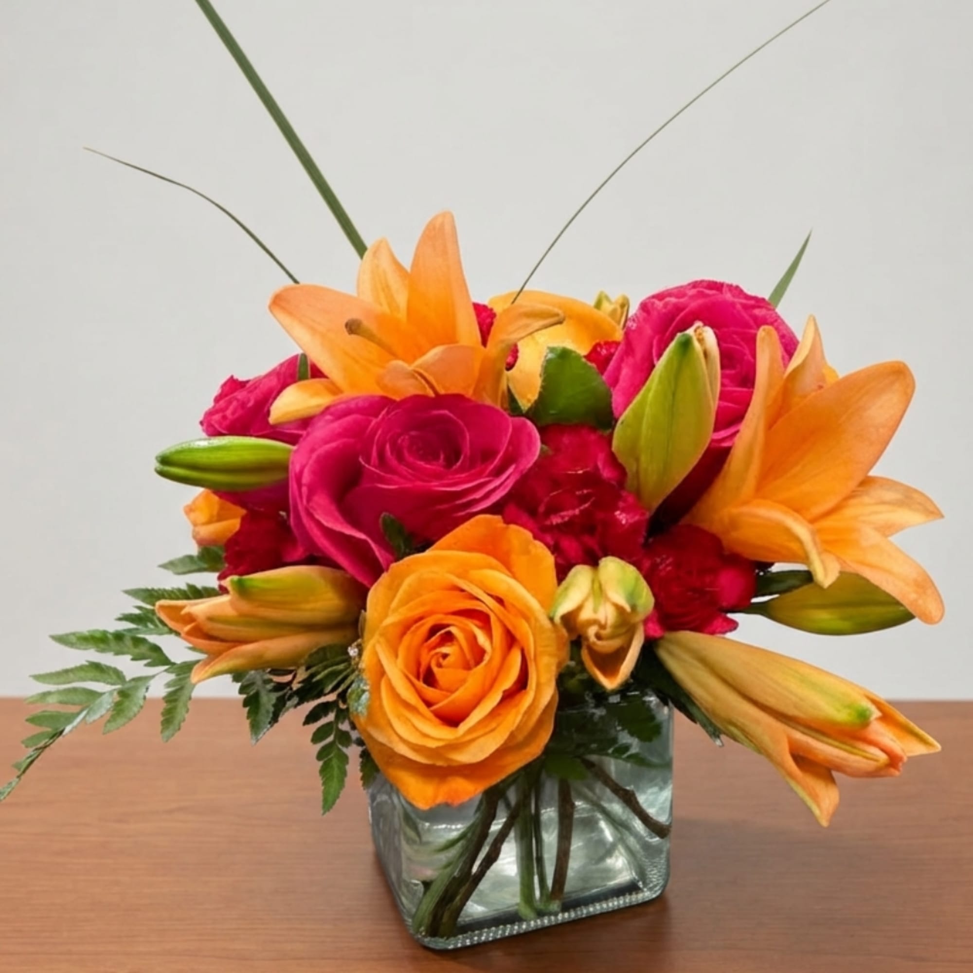 Orange lilies and pink roses arranged in a square glass vase, photo 2 of 4
