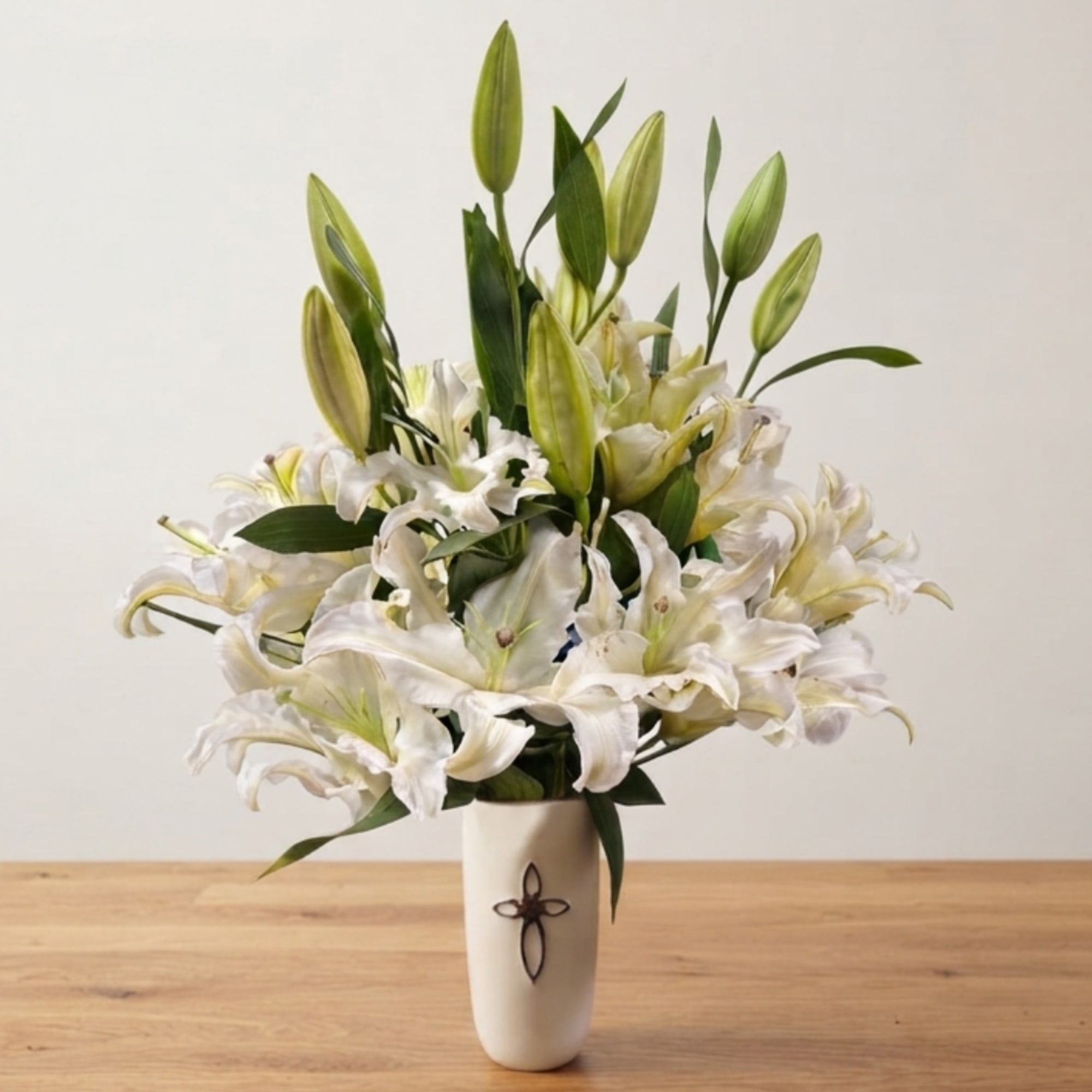 White lilies arranged in a tall cream vase on a wooden table