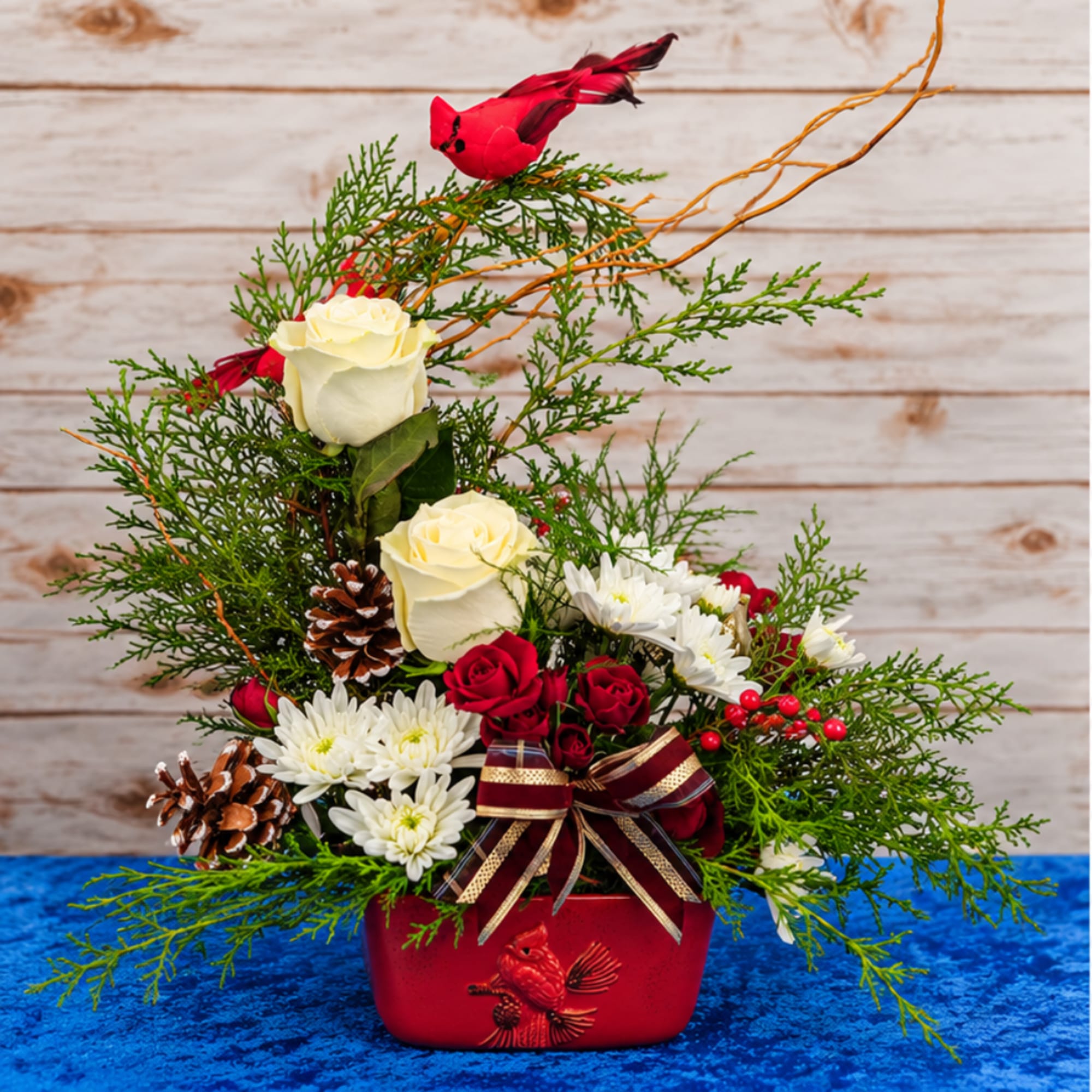 Holiday floral arrangement in a red vase with roses, daisies, and pinecones