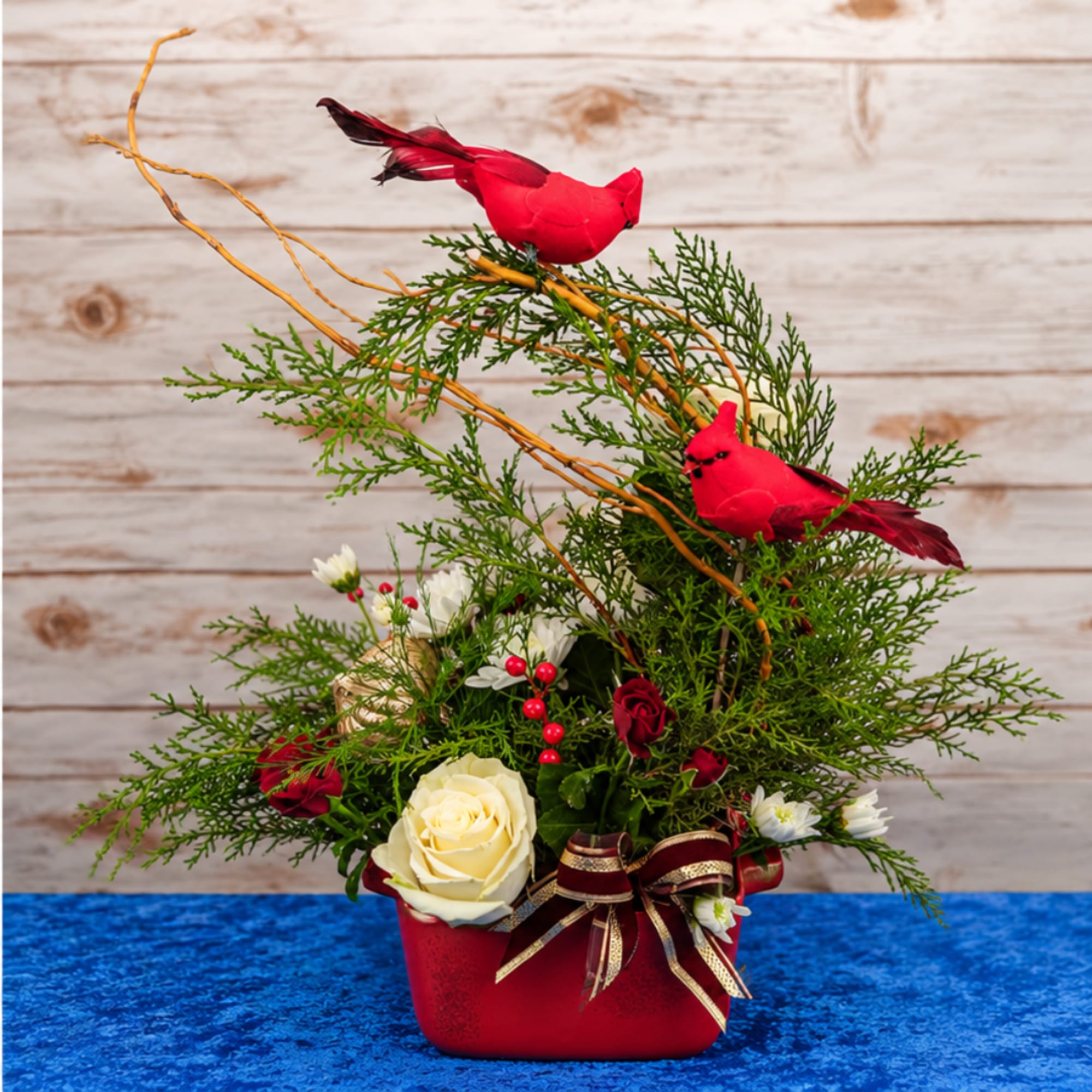 Red bird figurines in a floral arrangement with roses in a red container
