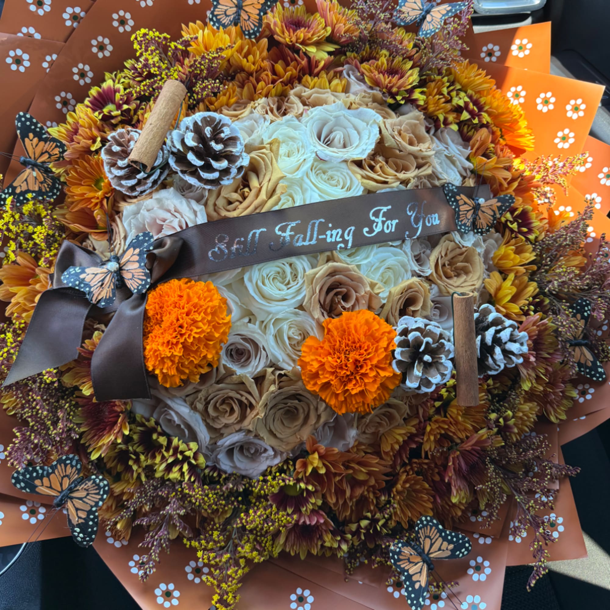 Round bouquet of cream and tan roses with orange marigolds and butterflies