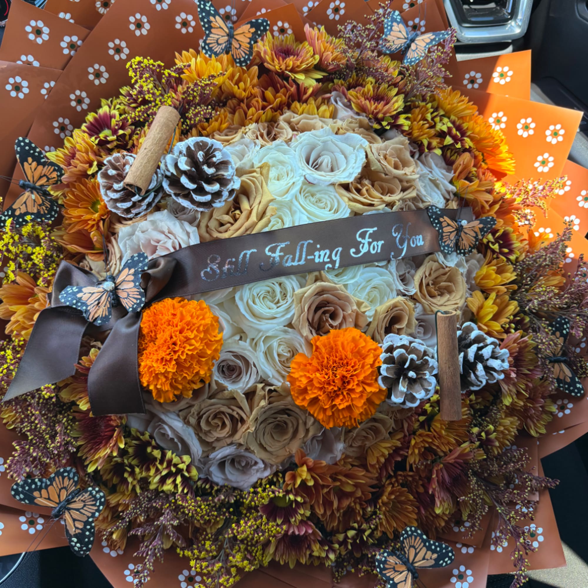 Round bouquet of cream and tan roses with orange marigolds and butterfly accents
