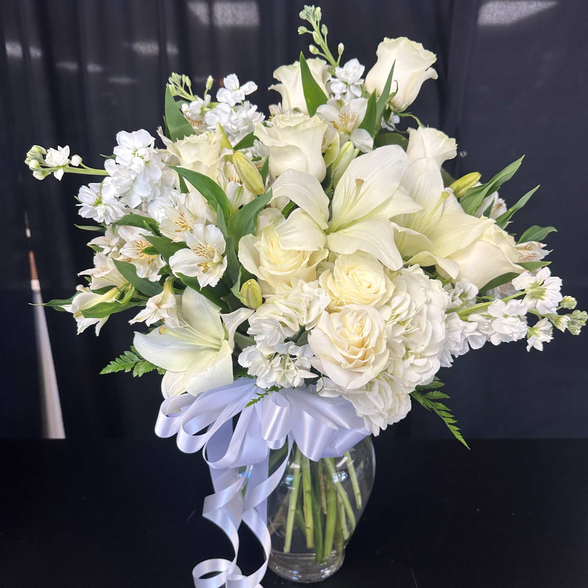 White floral bouquet in a clear glass vase with a lavender ribbon