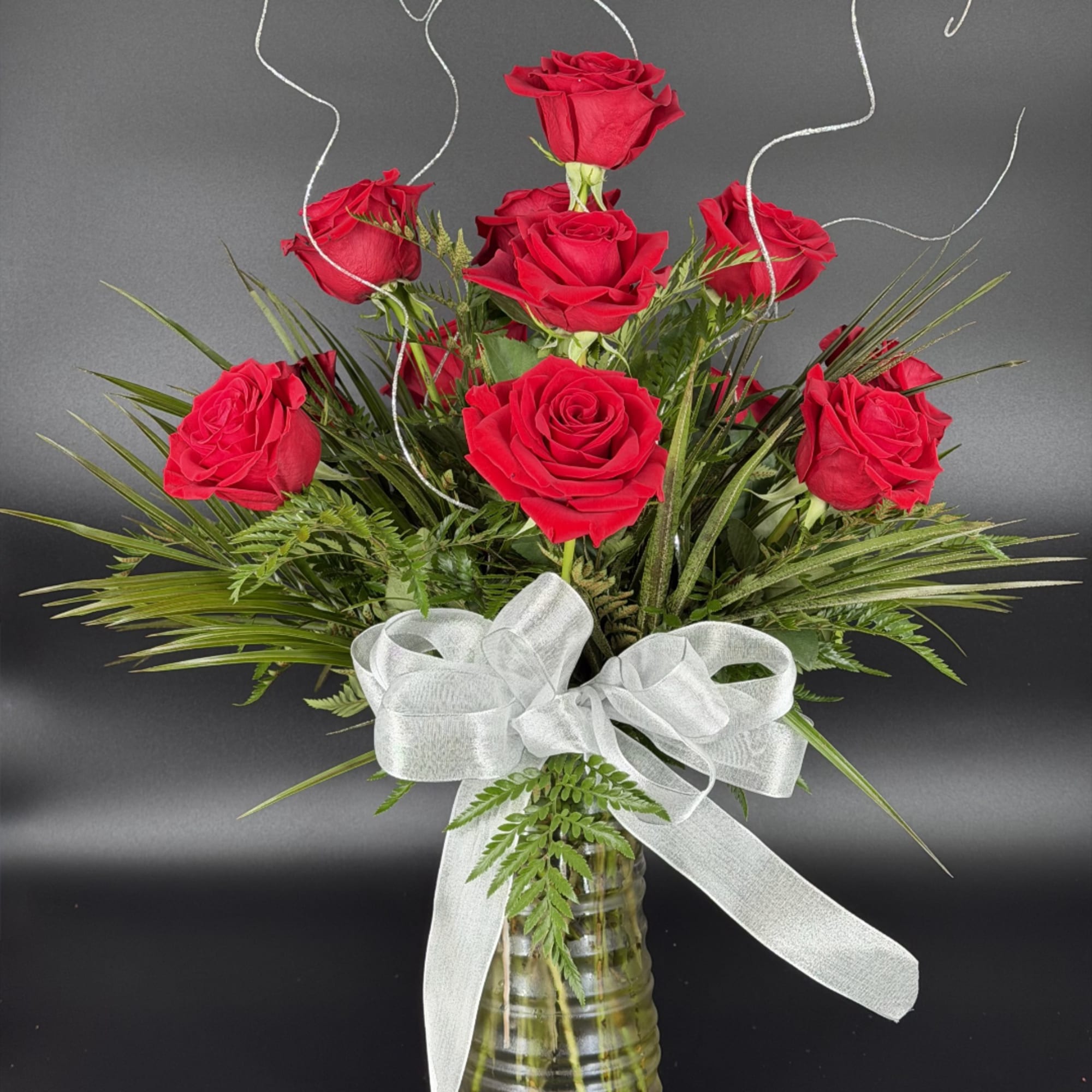 Red roses arranged in a glass vase with a white ribbon