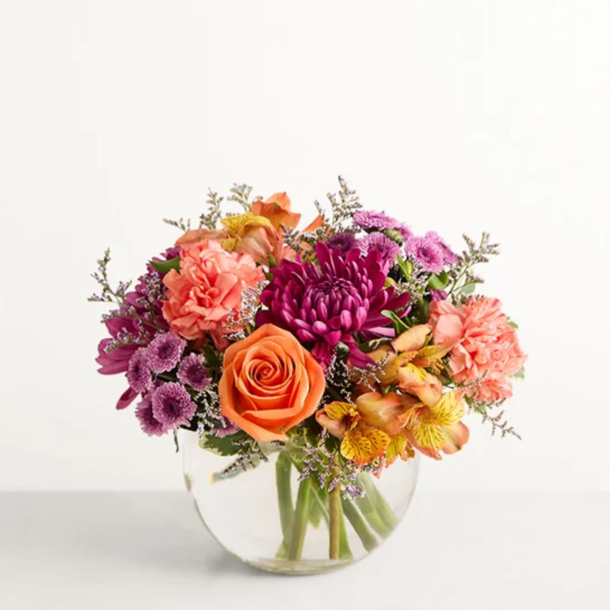Mixed bouquet of orange, pink, and purple flowers in a clear glass vase
