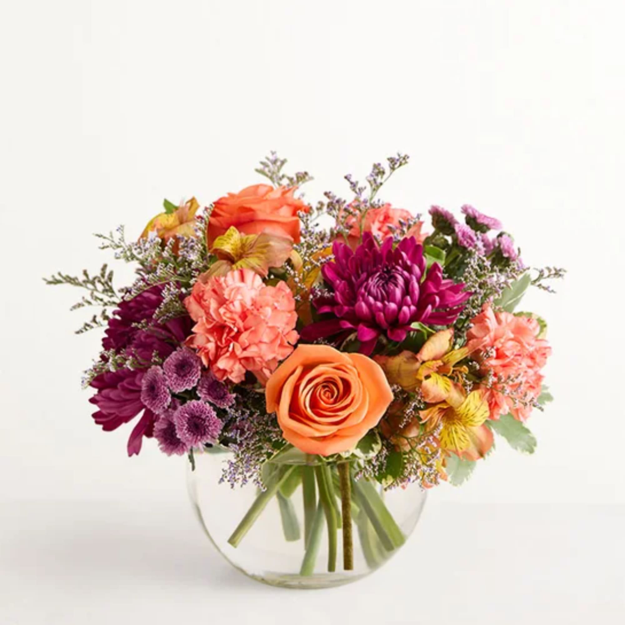 Mixed bouquet of orange, pink, and purple flowers in a clear glass vase