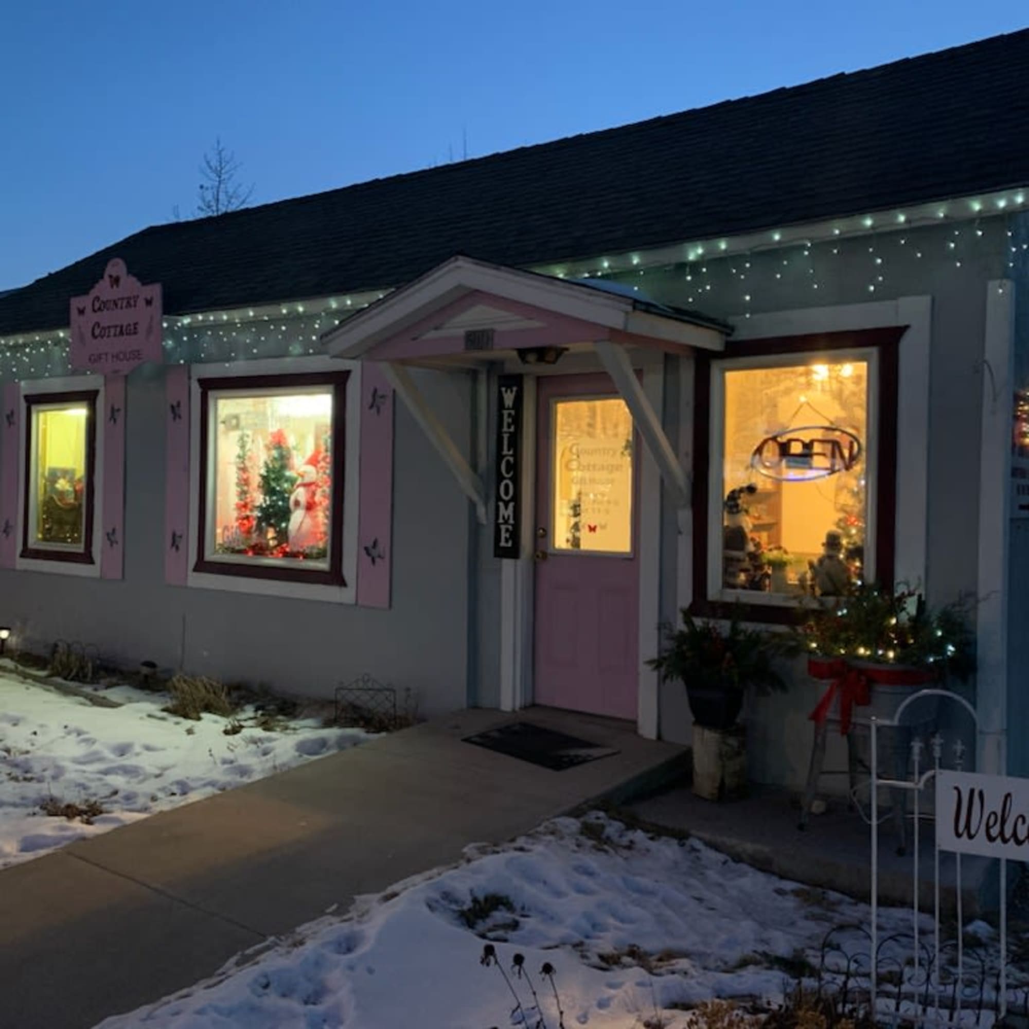 A small cottage storefront decorated with Christmas lights and a welcome sign
