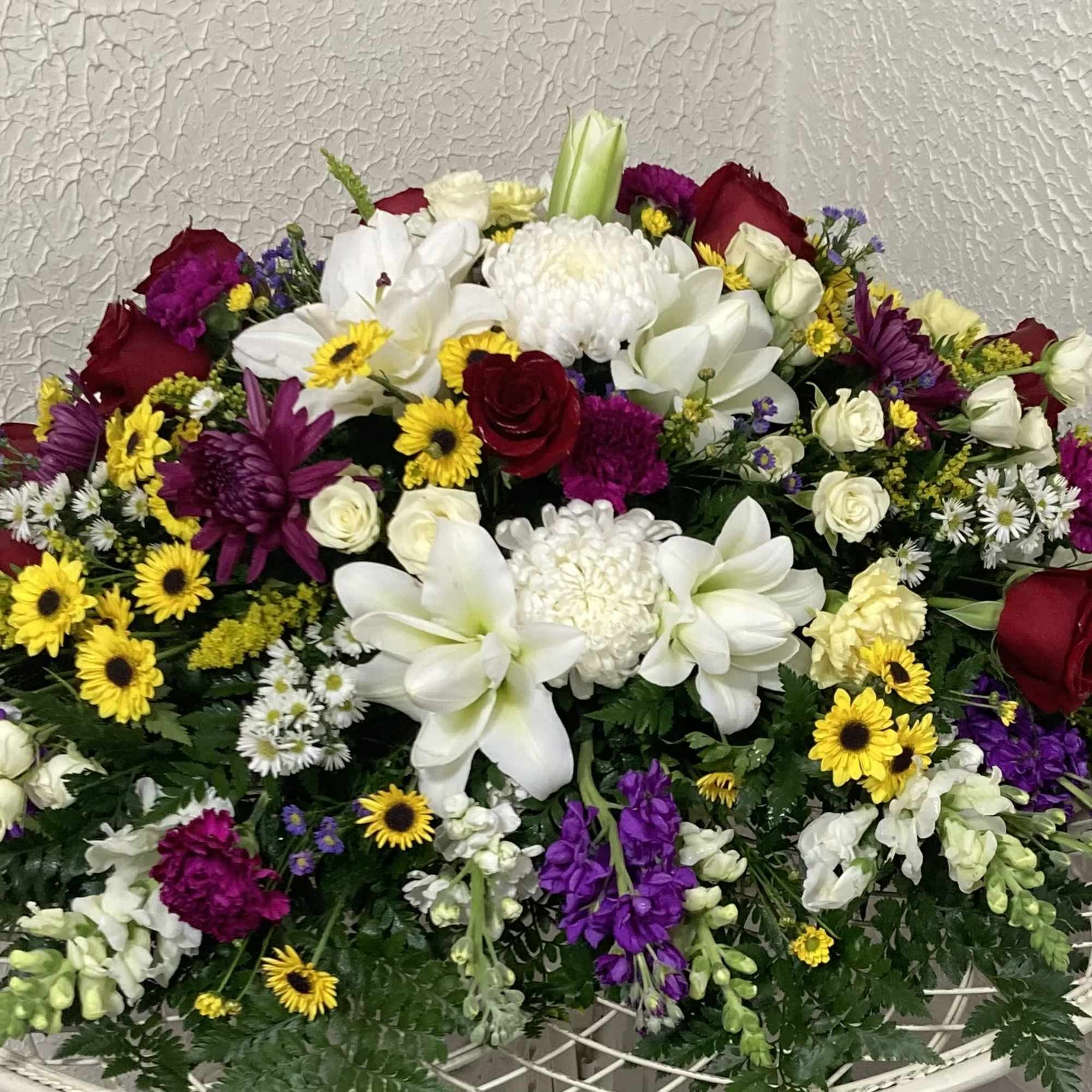 Large mixed floral arrangement with white lilies, red roses, and purple flowers
