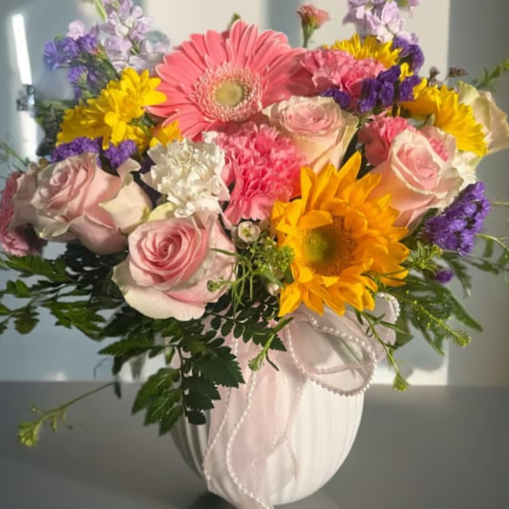 Mixed bouquet of pink roses, gerbera daisies, and sunflowers in a white vase