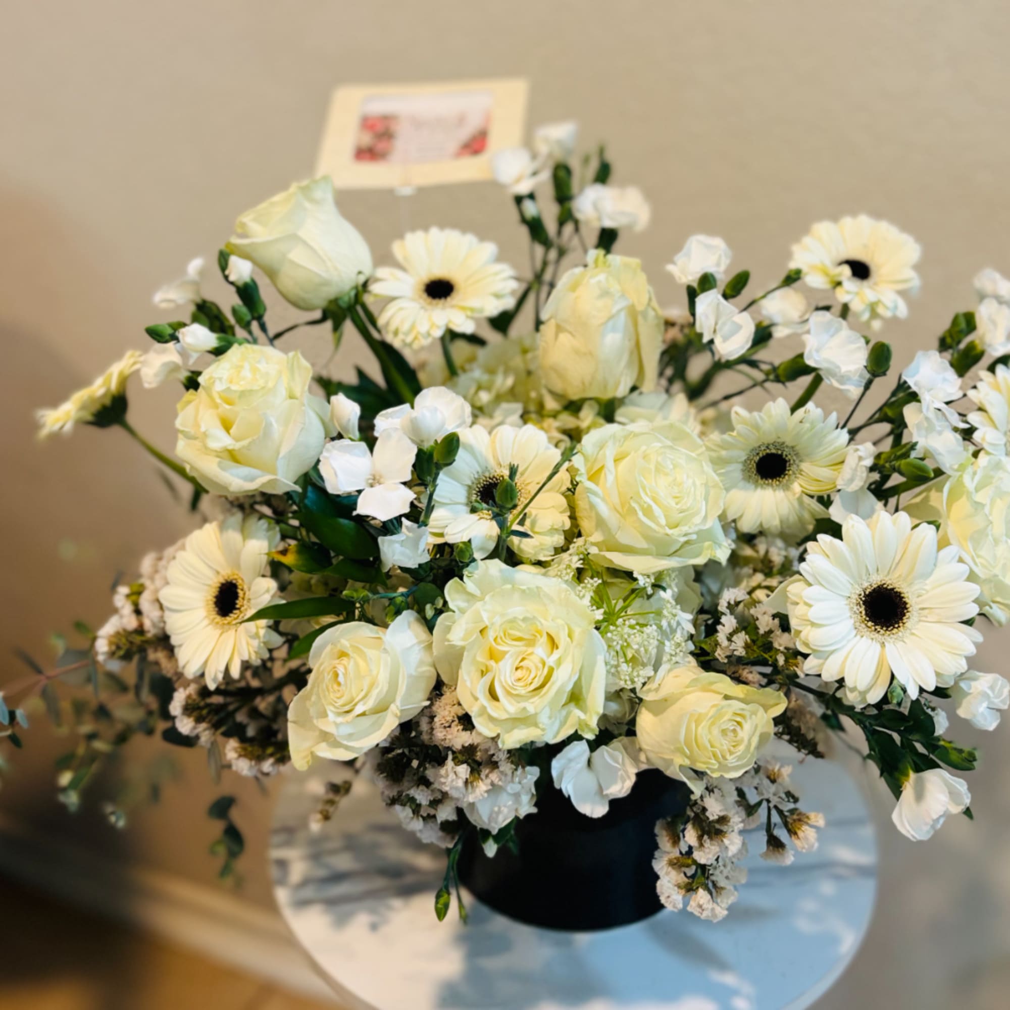 Cream roses and white daisies arranged in a black vase
