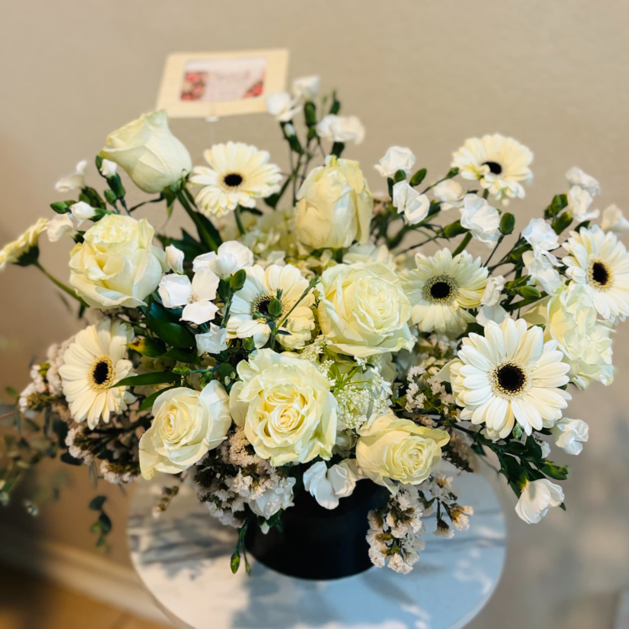 White roses and gerbera daisies arranged in a black vase
