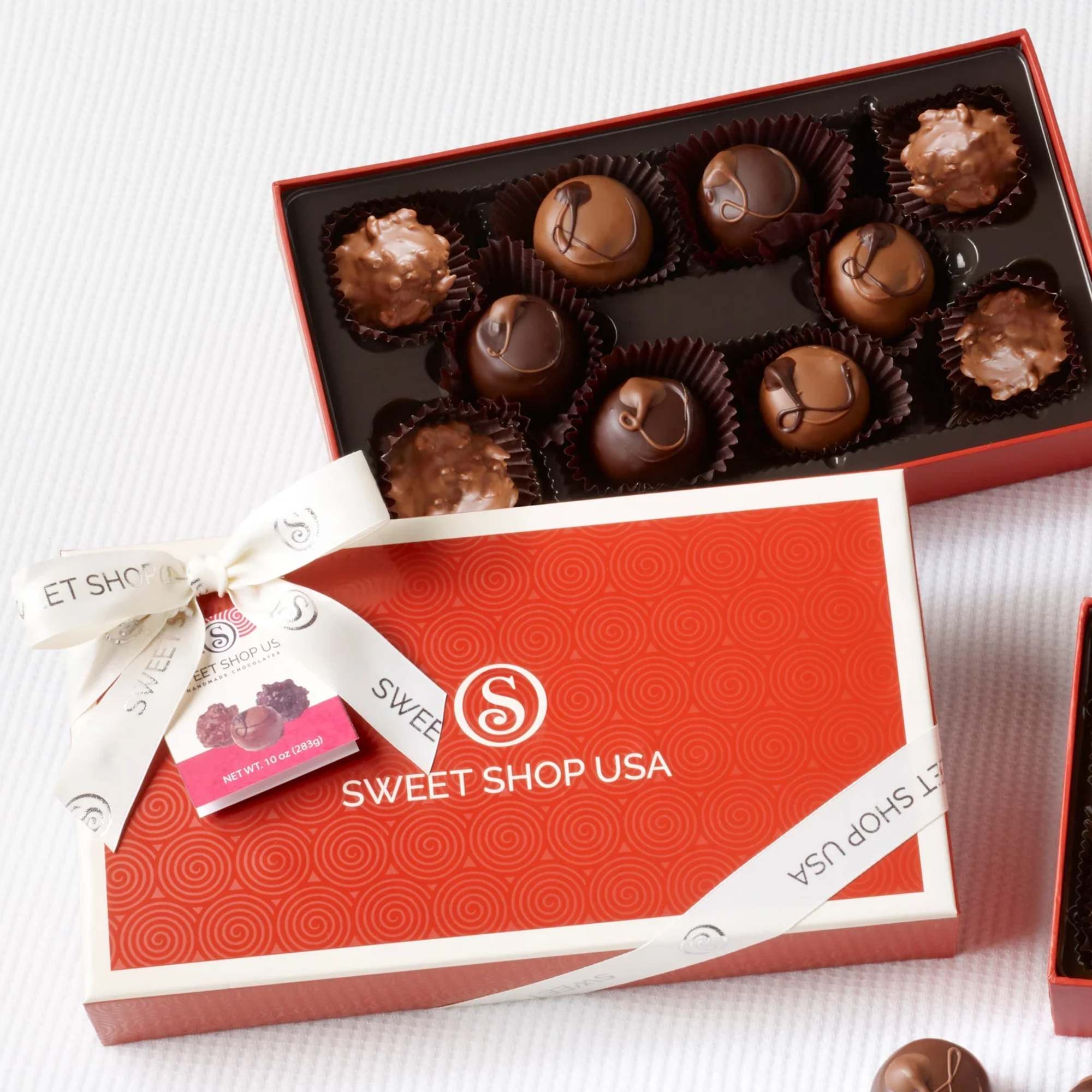 Open orange gift box of assorted chocolate truffles with matching lid and ribbon on a white surface