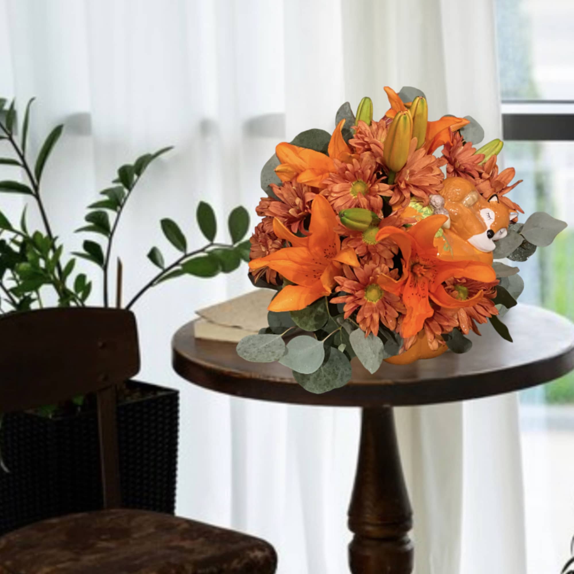 Orange lilies and mums arranged in a pumpkin-shaped container with a small fox figurine