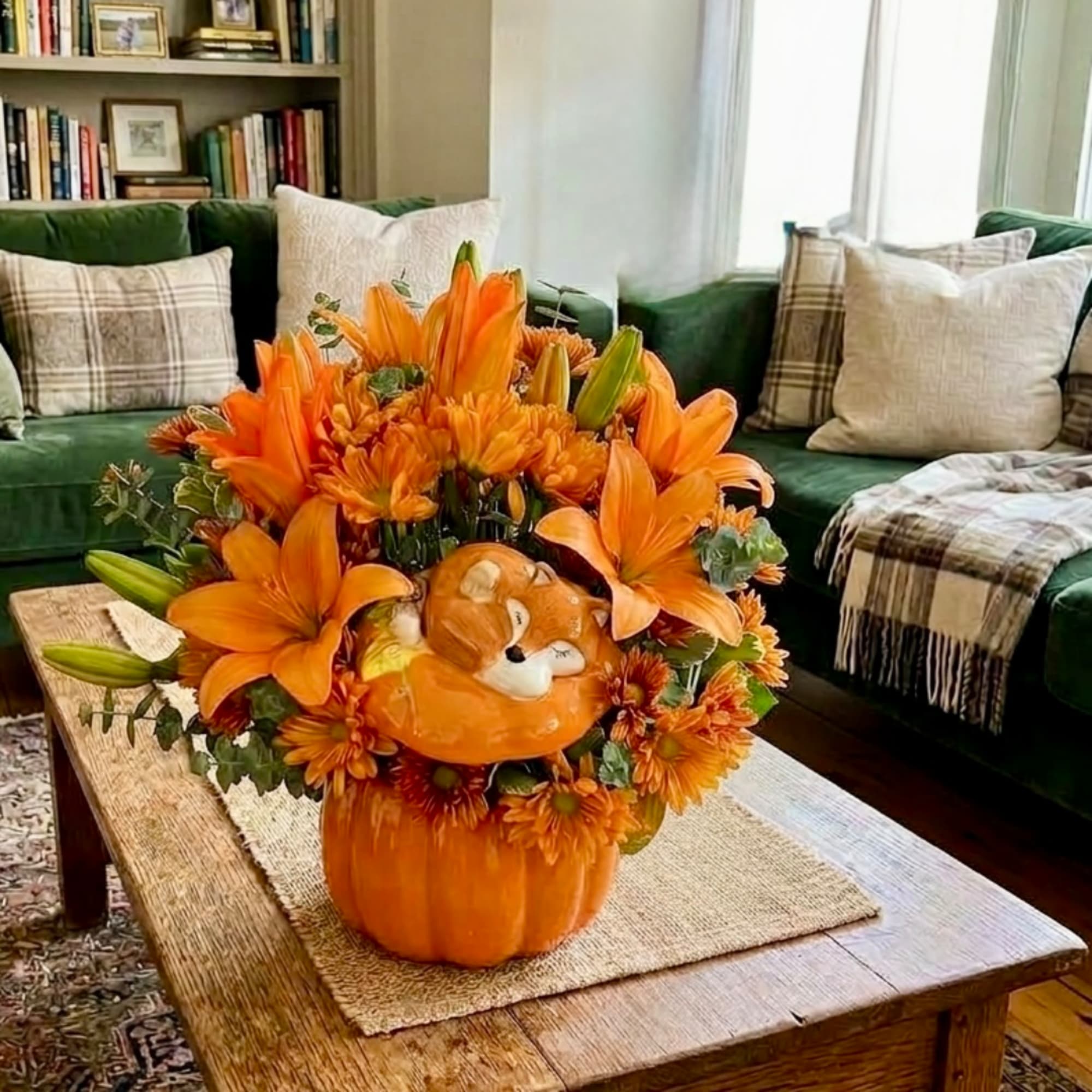Orange floral arrangement in a pumpkin container with a small cat face decoration