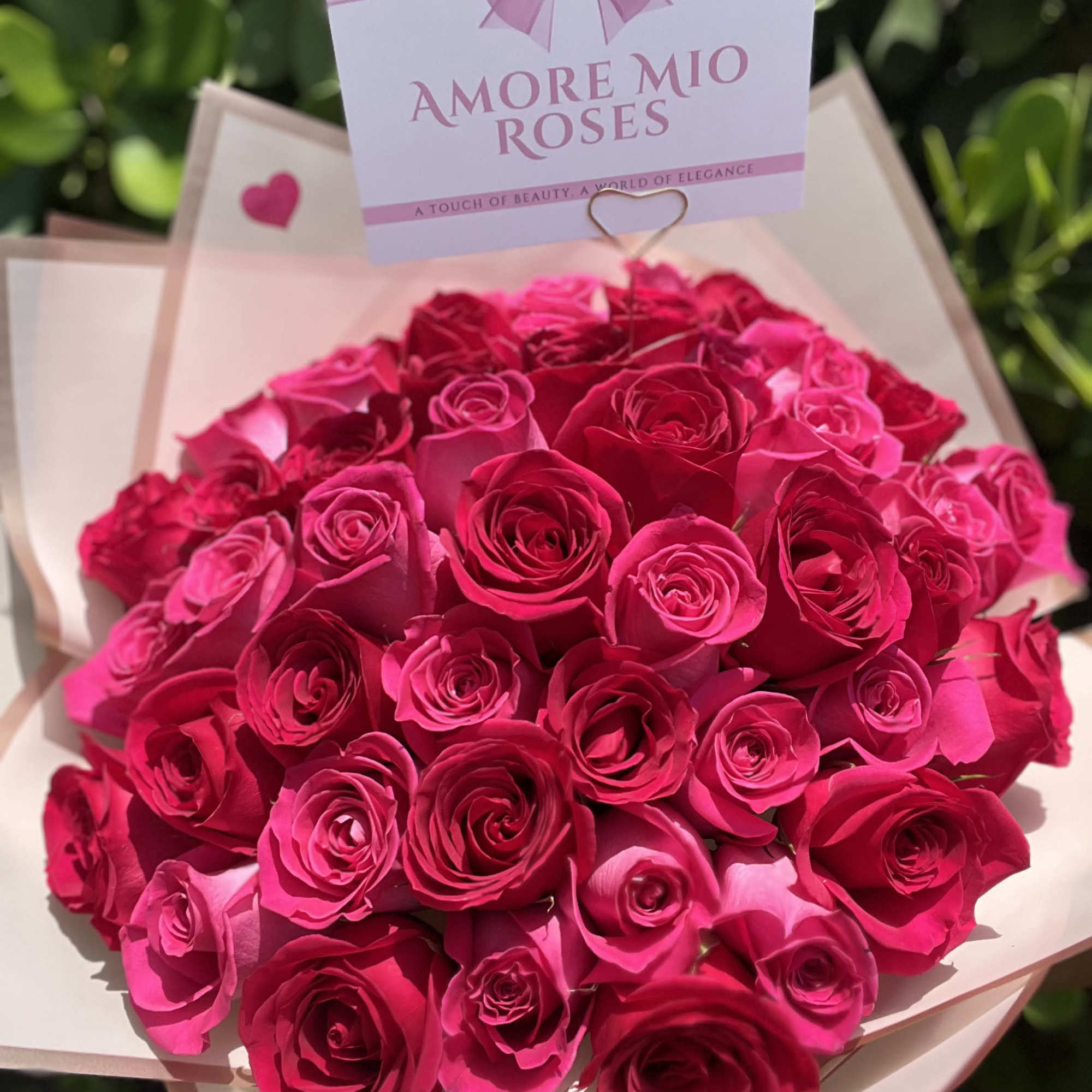 Bouquet of bright pink roses wrapped in pale paper with a gift card