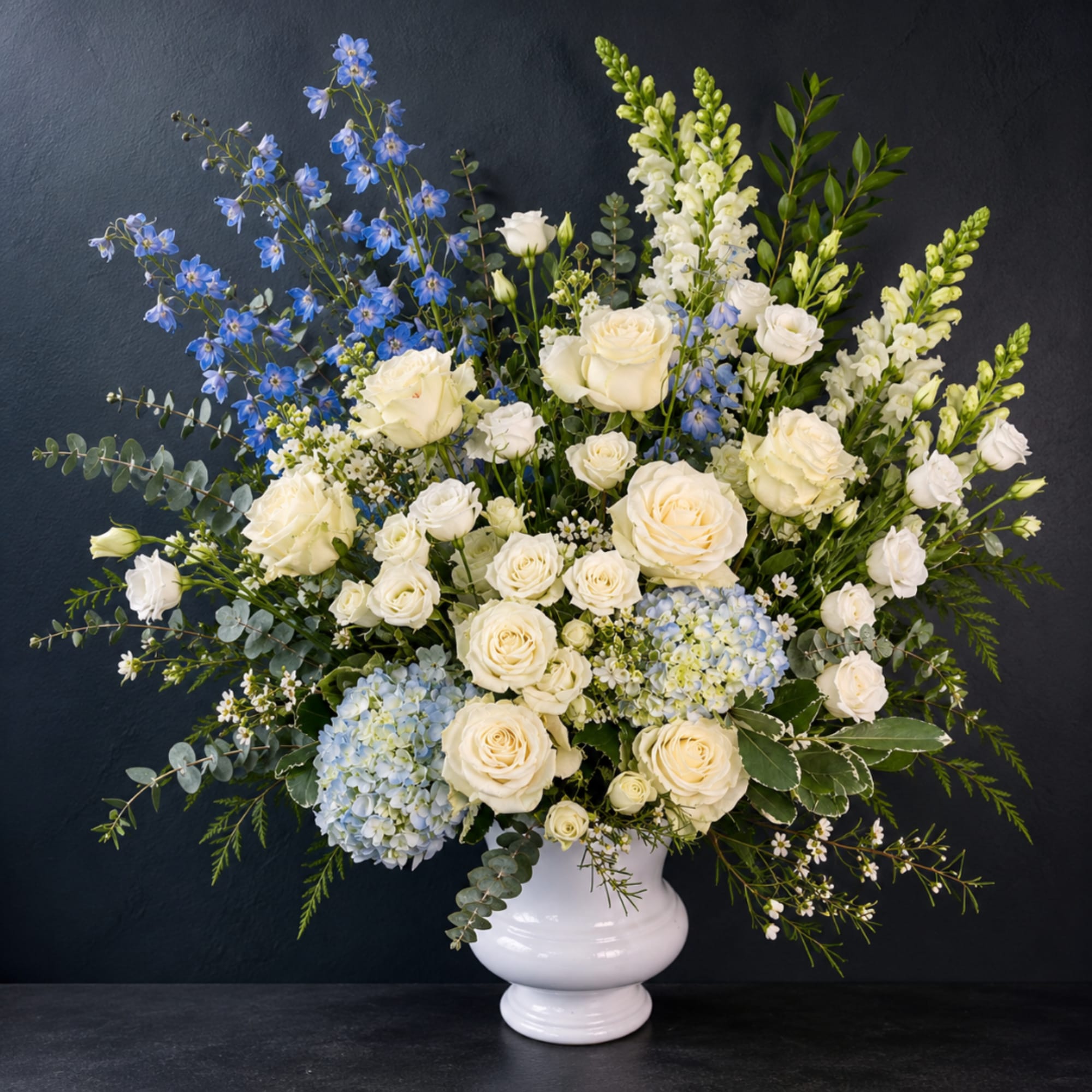 White roses and blue flowers arranged in a white vase