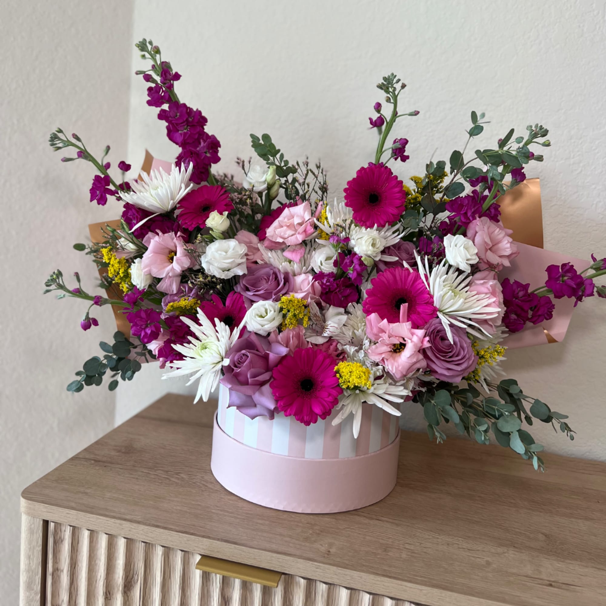 Pink and white mixed flower arrangement in a striped round box