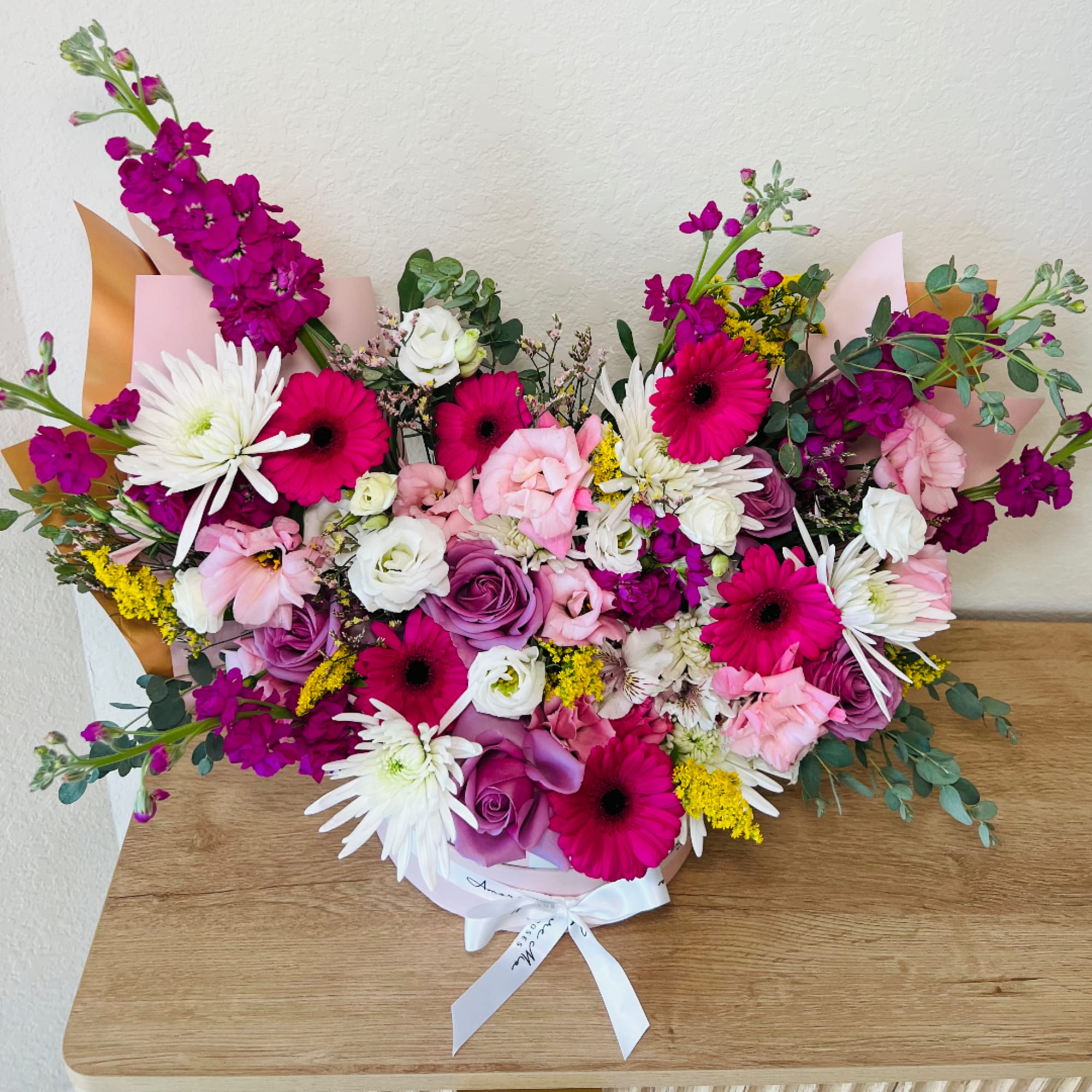 Mixed bouquet of pink, white, and purple flowers in a pink box with ribbon