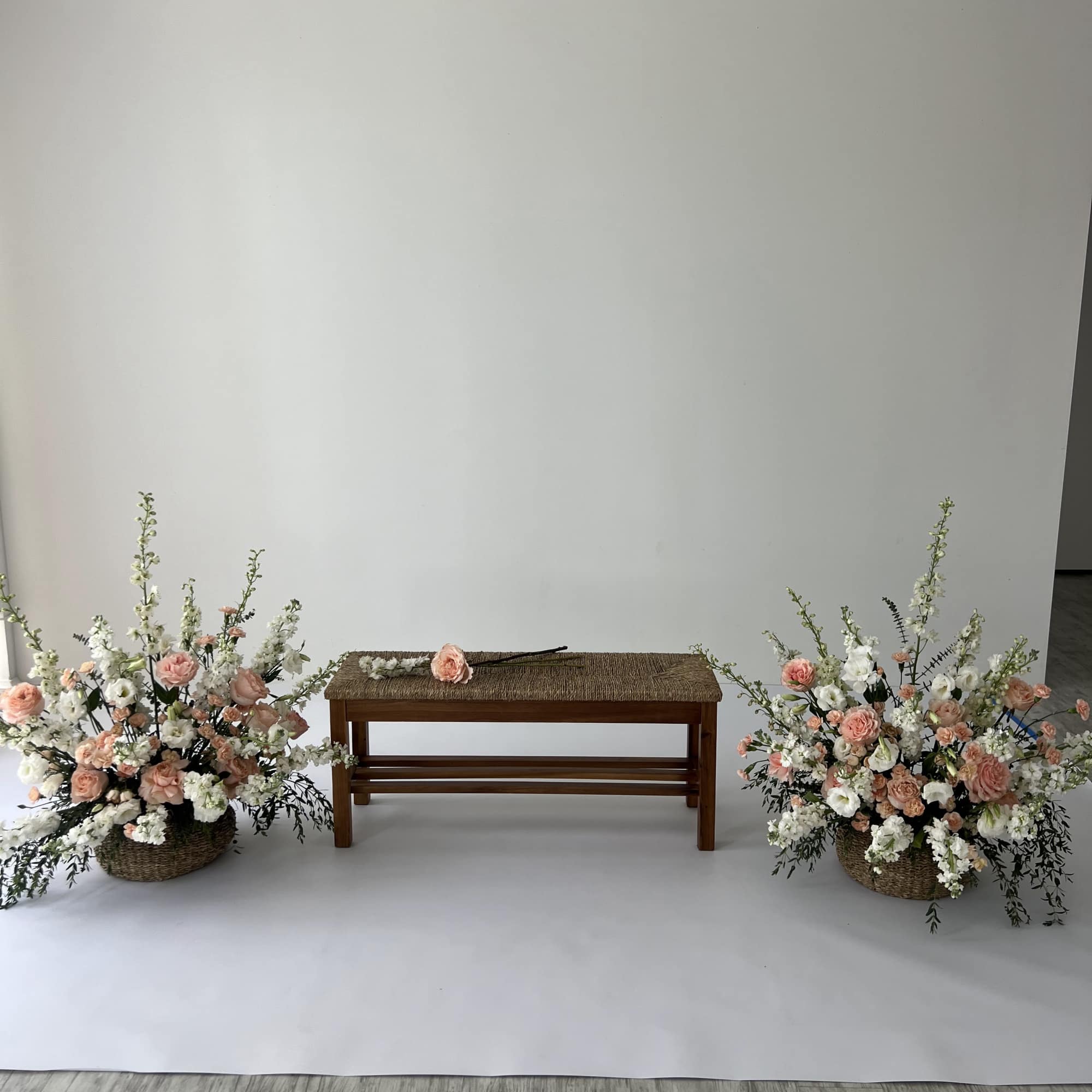 Two floral arrangements flank a wooden bench with a single rose on top