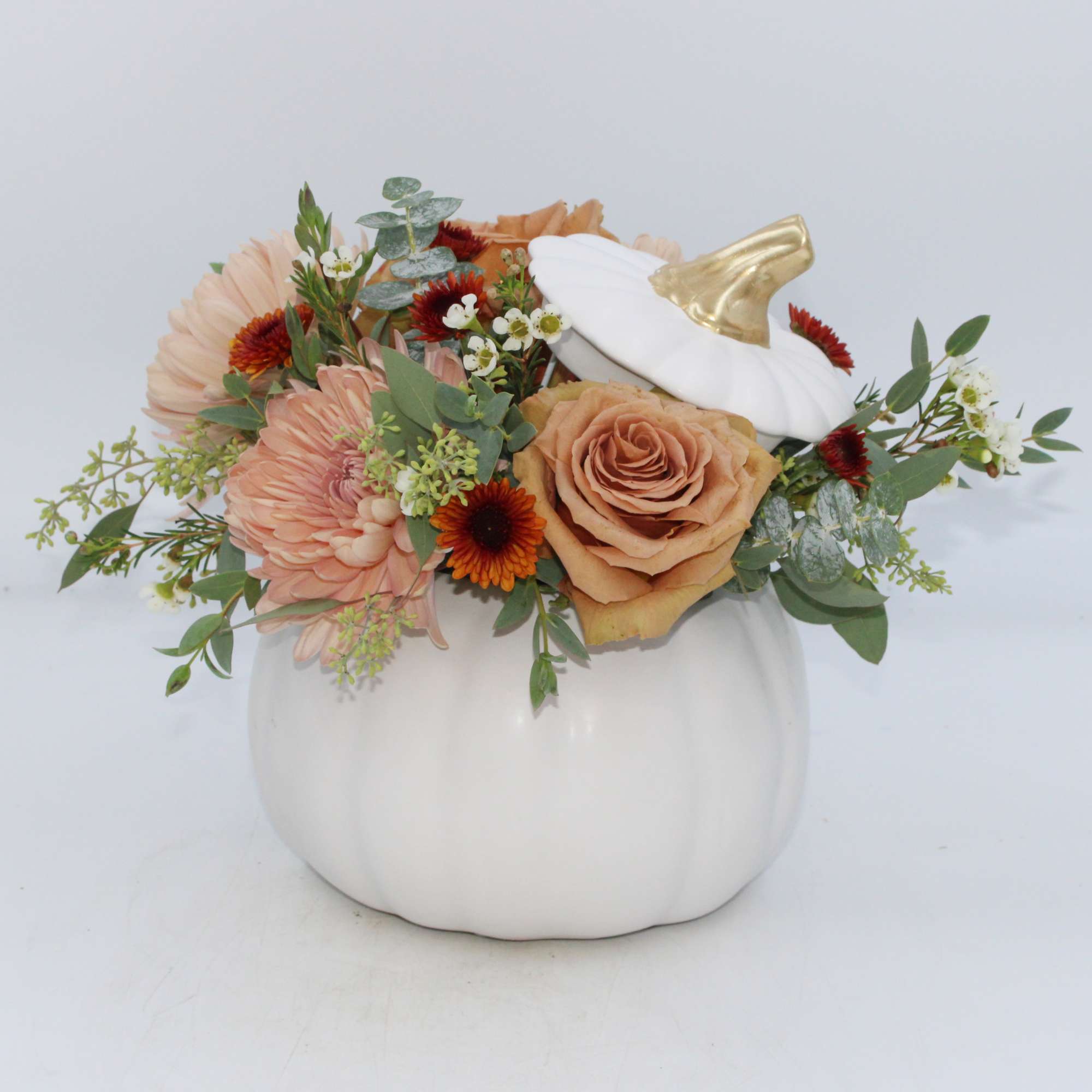 Floral arrangement in a white pumpkin container with peach and orange blooms