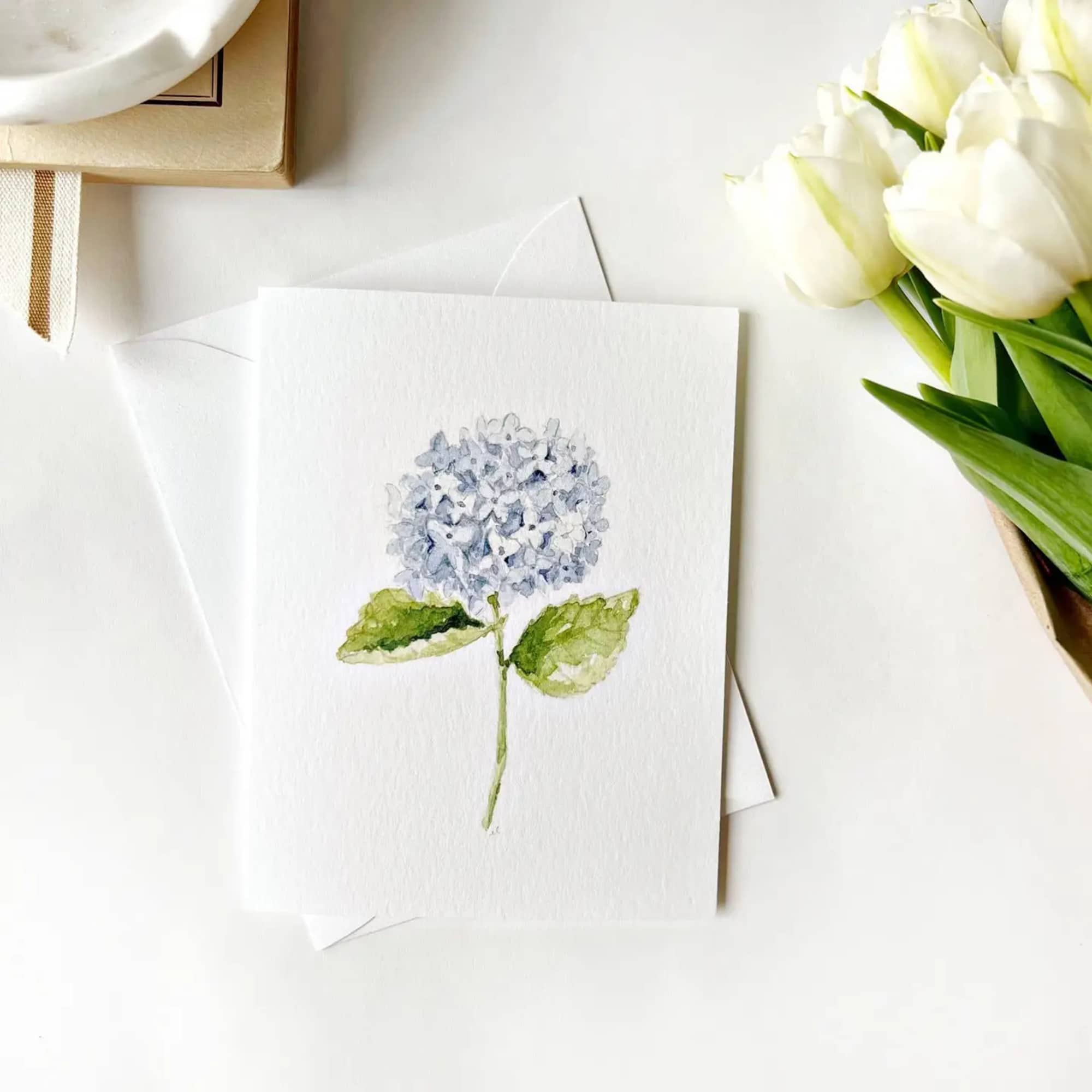 Watercolor card with a blue hydrangea bloom and white tulips beside it