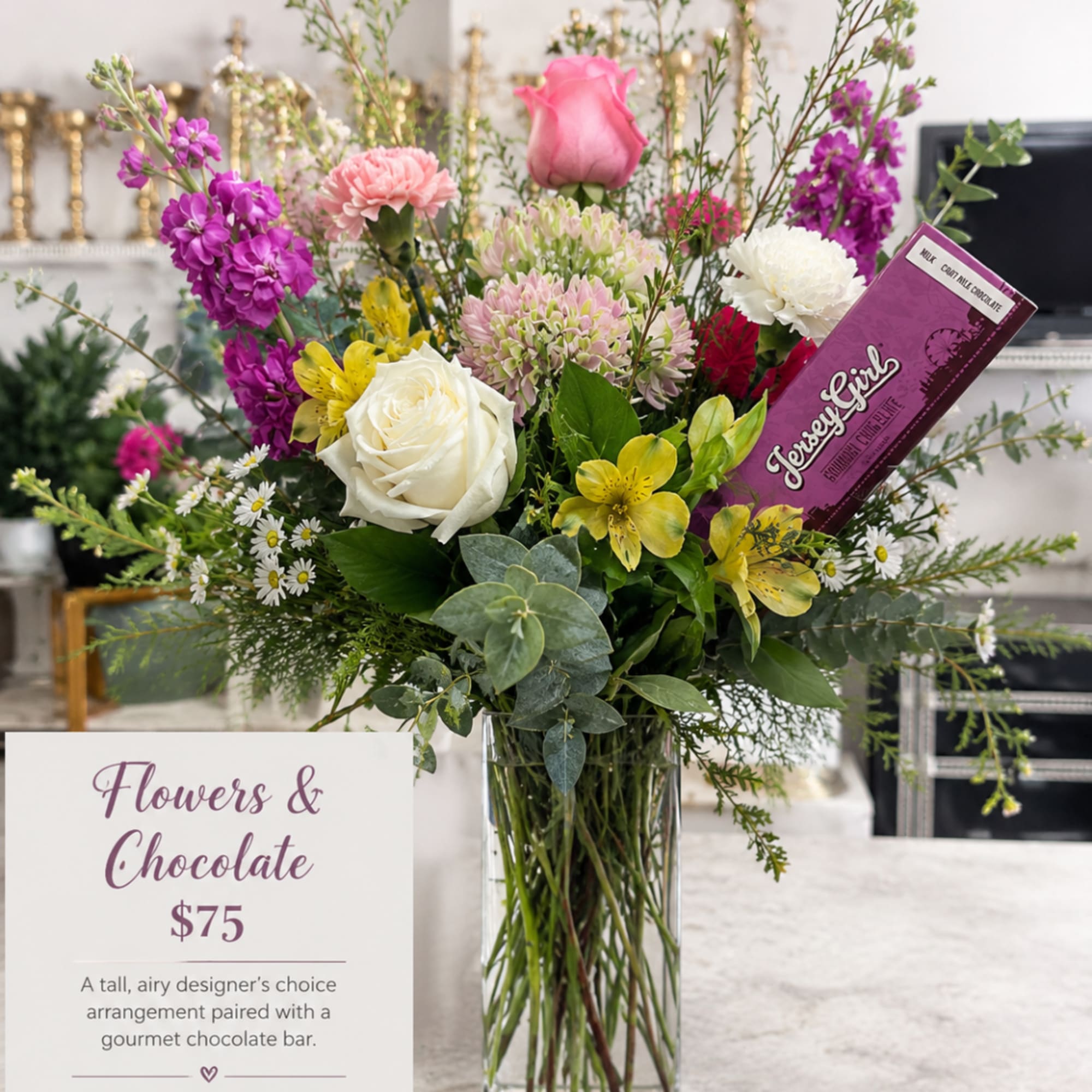 Tall mixed bouquet in a glass vase with a chocolate bar tucked in.