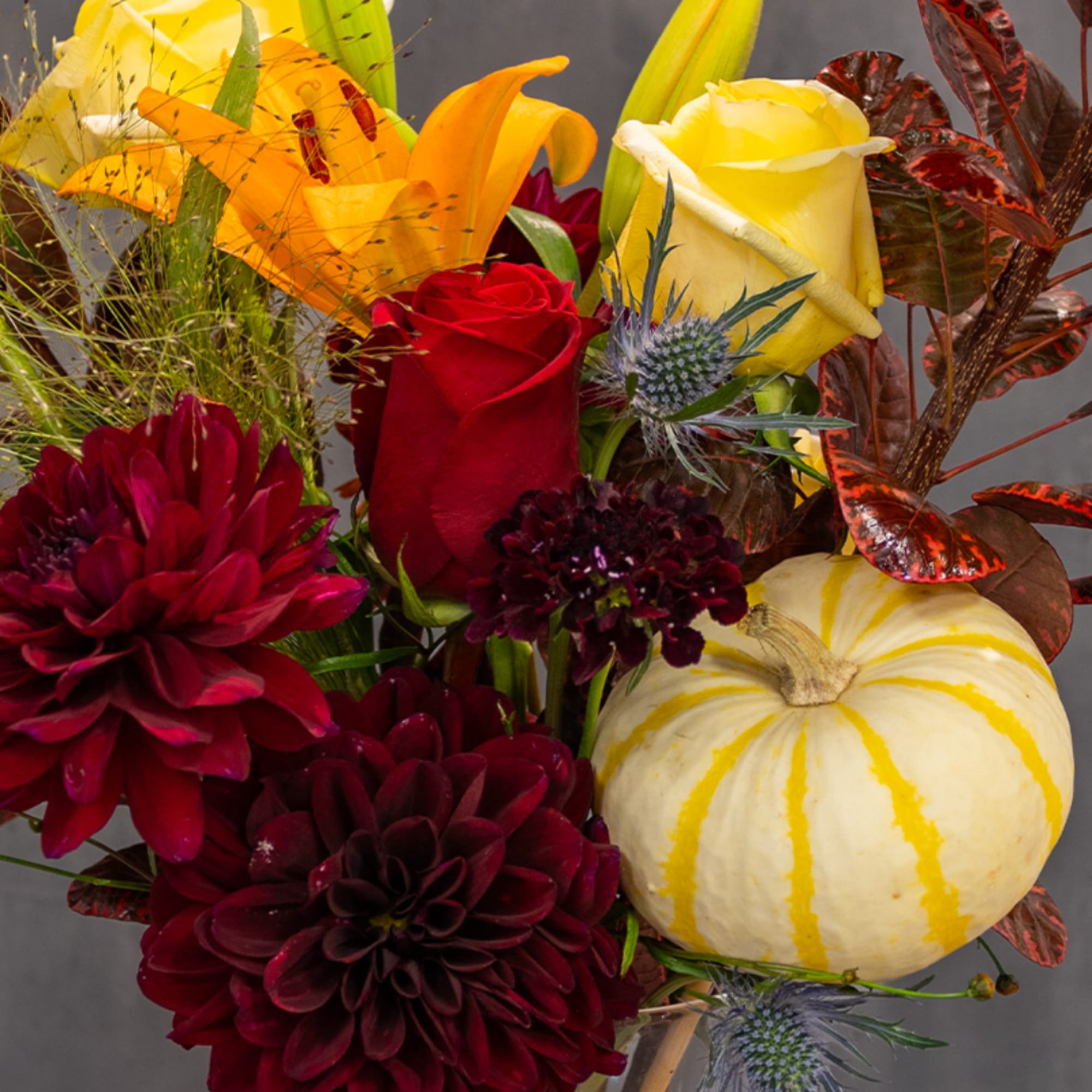Bouquet with red and yellow roses, orange lilies, and a striped pumpkin