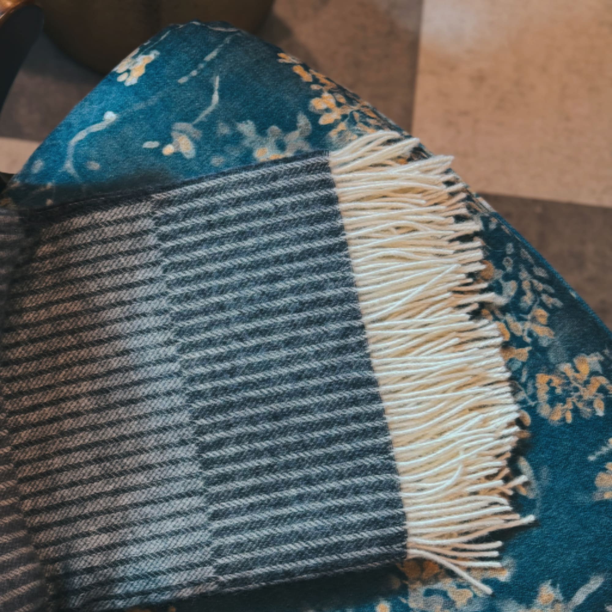 Folded blue patterned blanket with cream fringe on a chair
