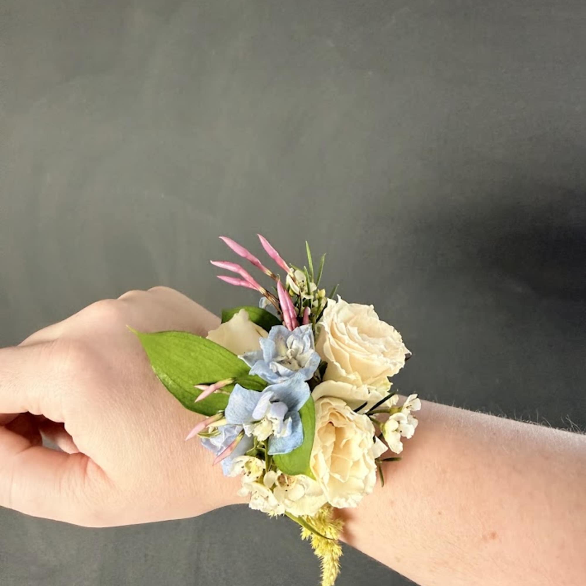 Small wrist corsage with cream roses, blue flowers, and pink accents