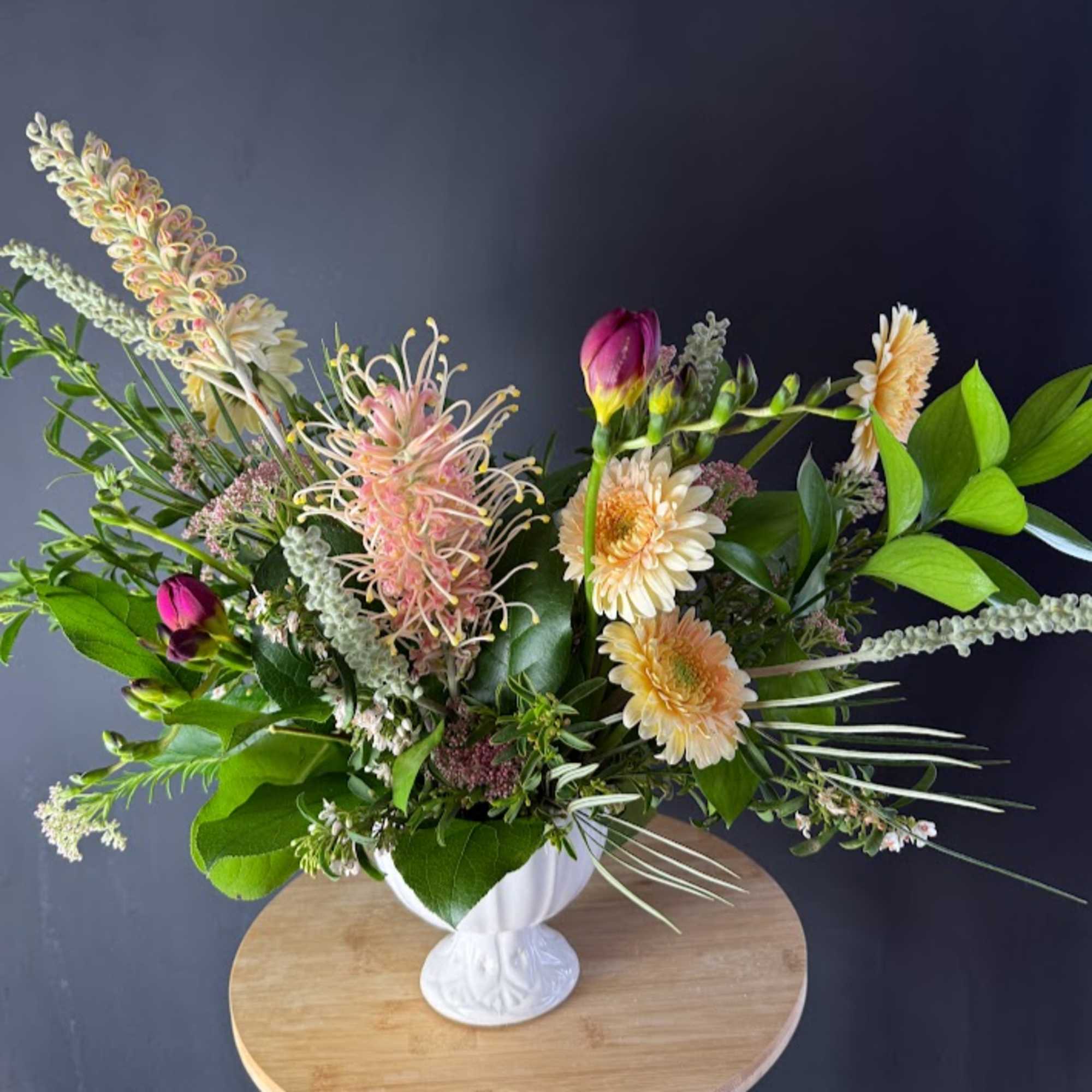 Mixed floral arrangement in a white pedestal vase with pink and cream blooms