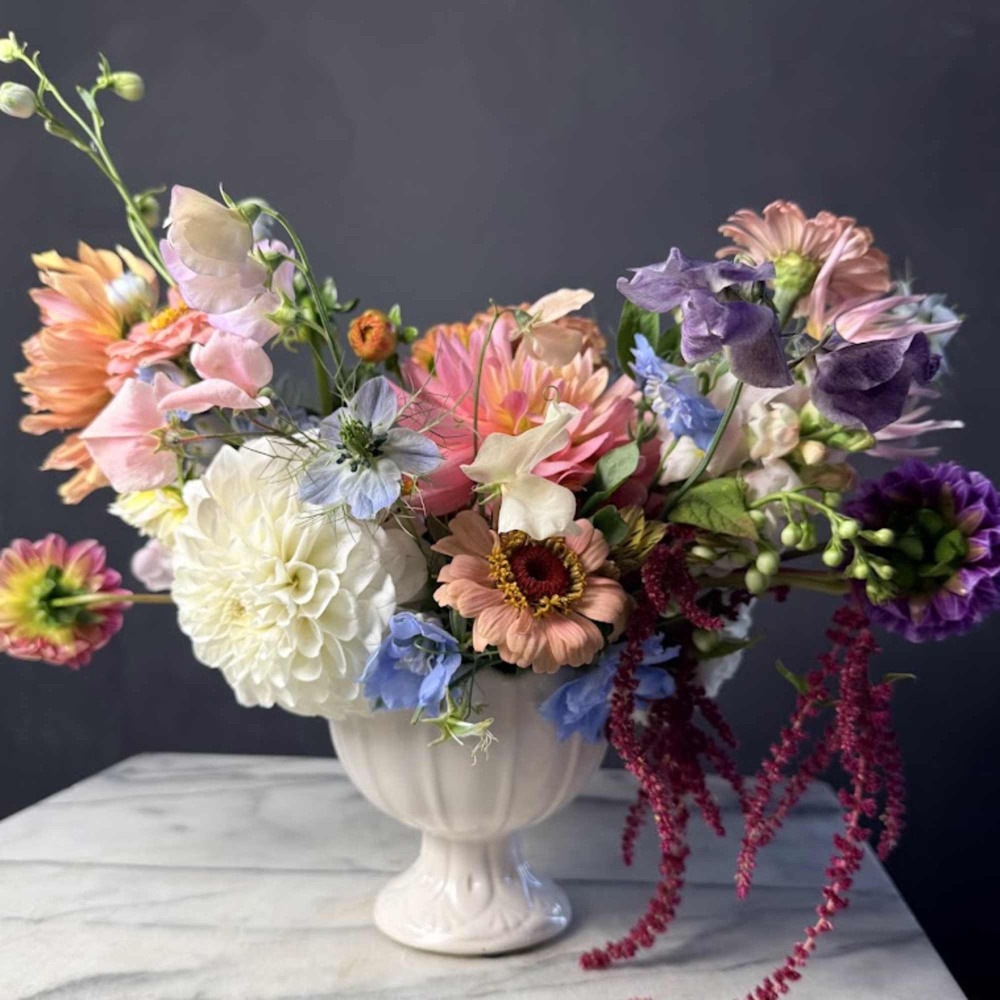 Mixed bouquet in a white pedestal vase with pink, purple, peach, and white flowers