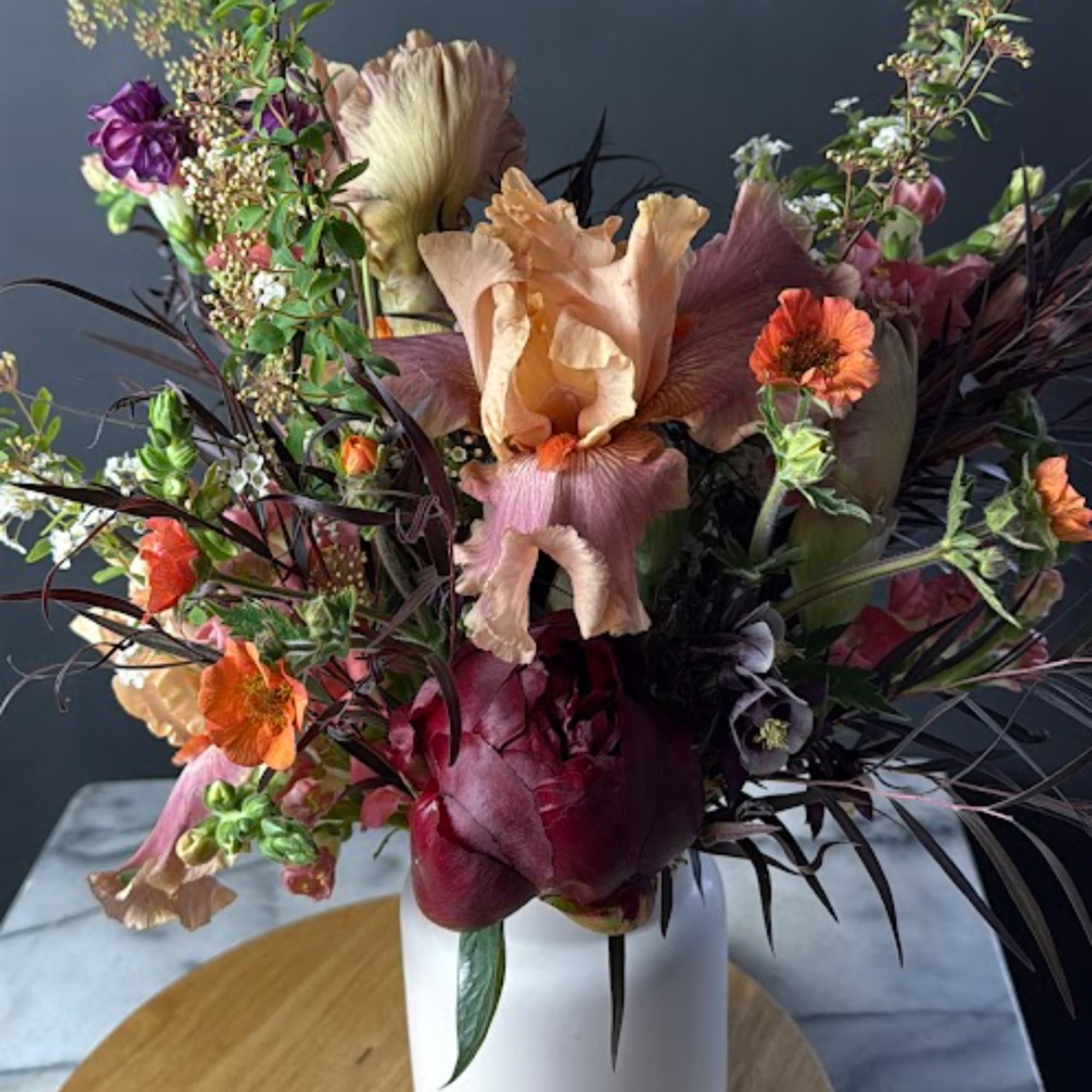 Mixed bouquet with peach, orange, and burgundy flowers in a white vase