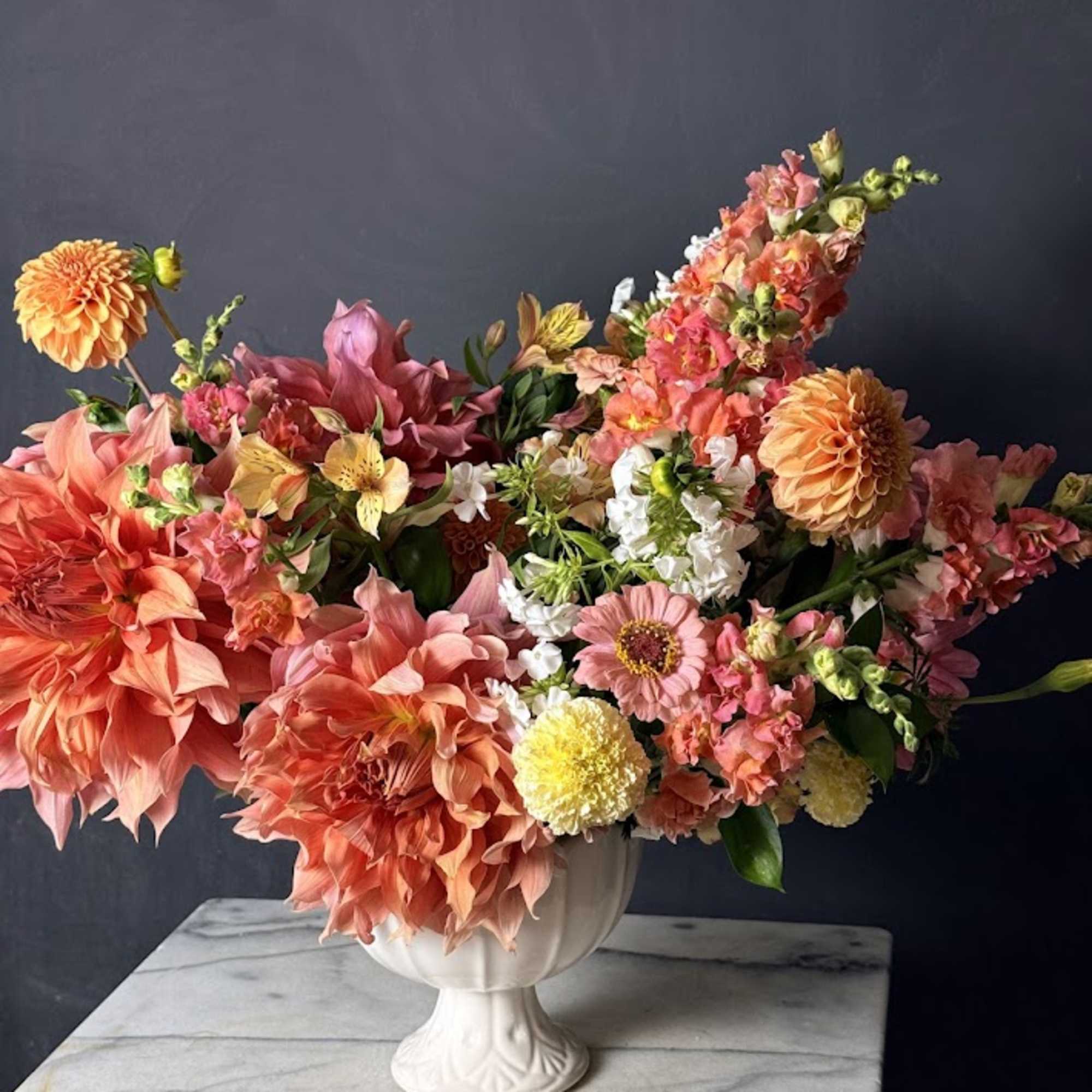 Large coral and pink flower arrangement in a white pedestal vase