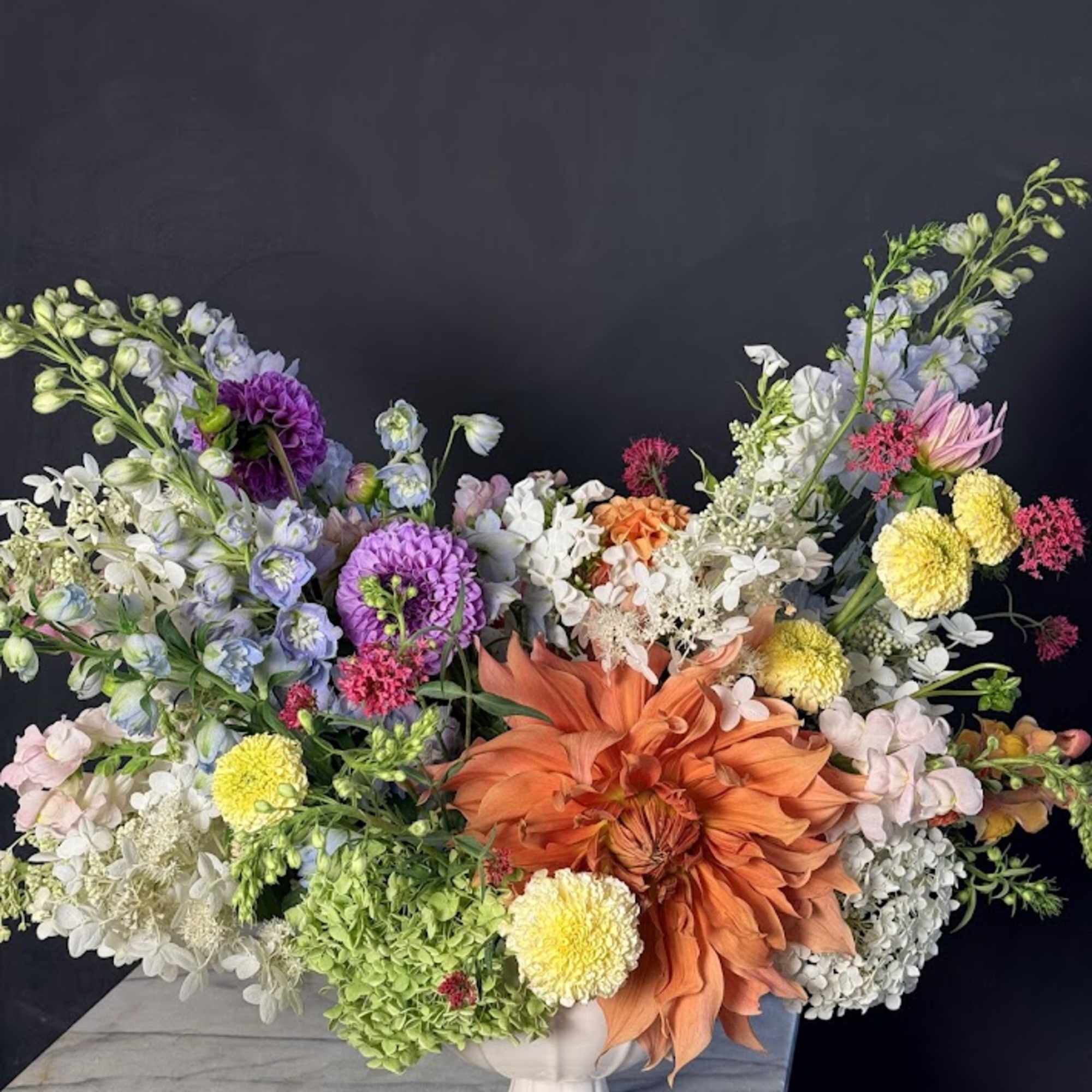 Large mixed flower arrangement in a white pedestal vase