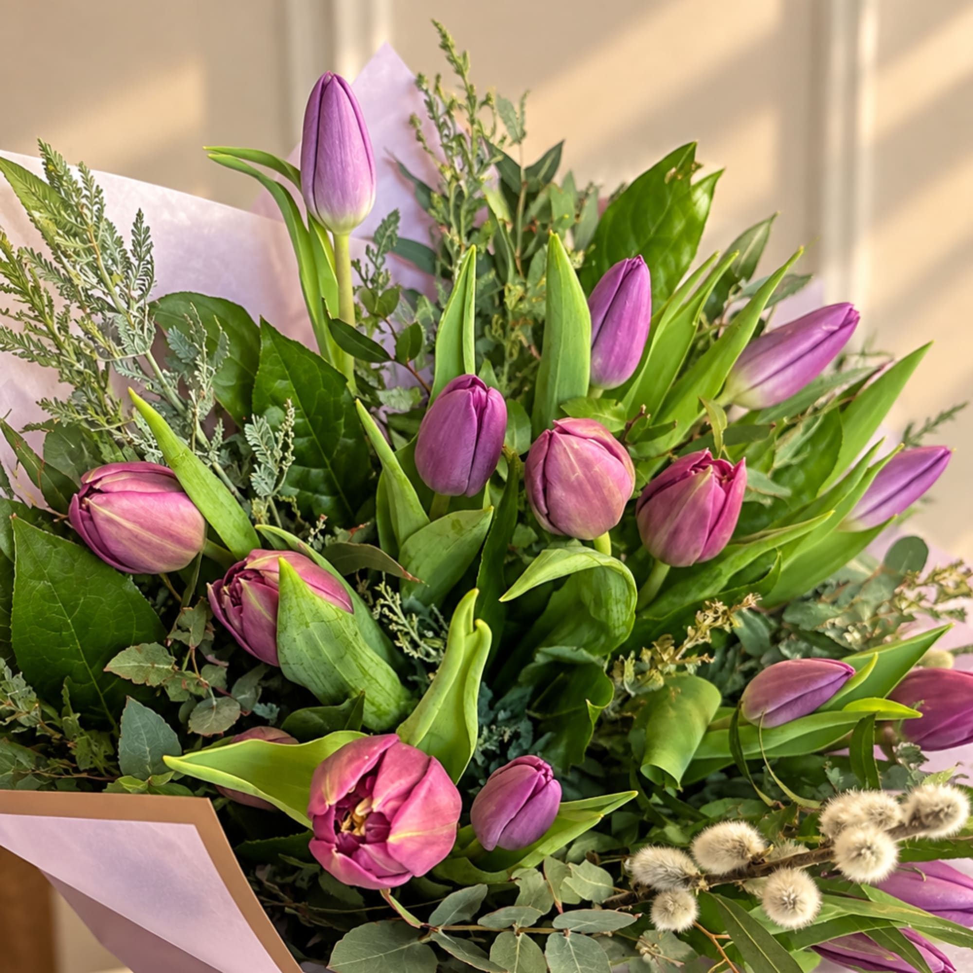 Bouquet of purple tulips with mixed greenery and pale wrapping paper